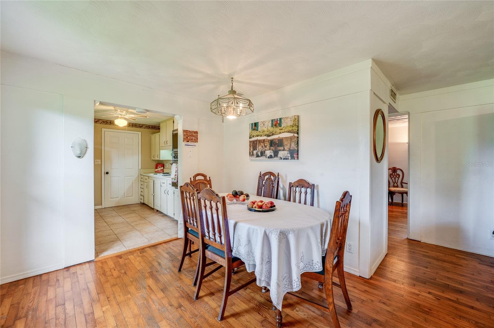 Dining area transitioning smoothly into the kitchen, complete with wood-look flooring, light walls, and tiled kitchen flooring beyond. A hanging overhead light fixture anchors the room while open doorways maintain an airy flow. - 1101 16TH ST, EDGEWATER
