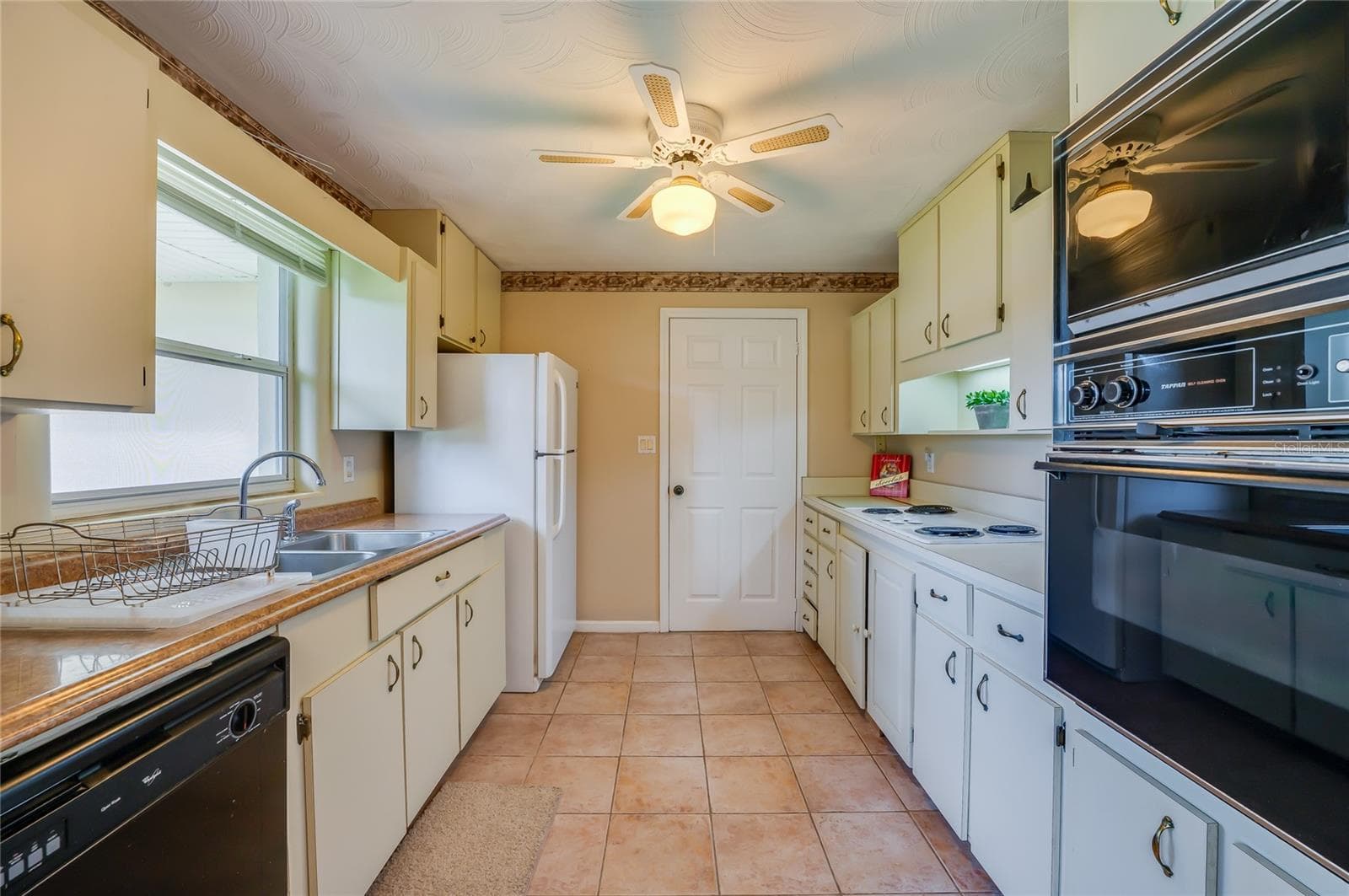 Functional galley-style kitchen featuring tile flooring, classic cabinetry, a double sink, and a built-in wall oven and microwave combo. - 1101 16TH ST, EDGEWATER