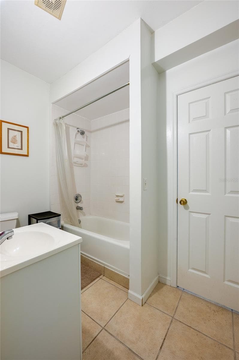 Clean bathroom area featuring a vanity sink, tiled floor, and a full bathtub with an overhead shower and curtain enclosure. - 1101 16TH ST, EDGEWATER