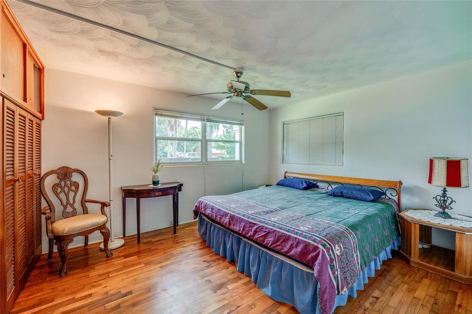 Spacious bedroom boasting rich hardwood floors, textured ceilings, a central ceiling fan, and extensive floor-to-ceiling built-in closets. Double windows invite soft natural light into the room. - 1101 16TH ST, EDGEWATER