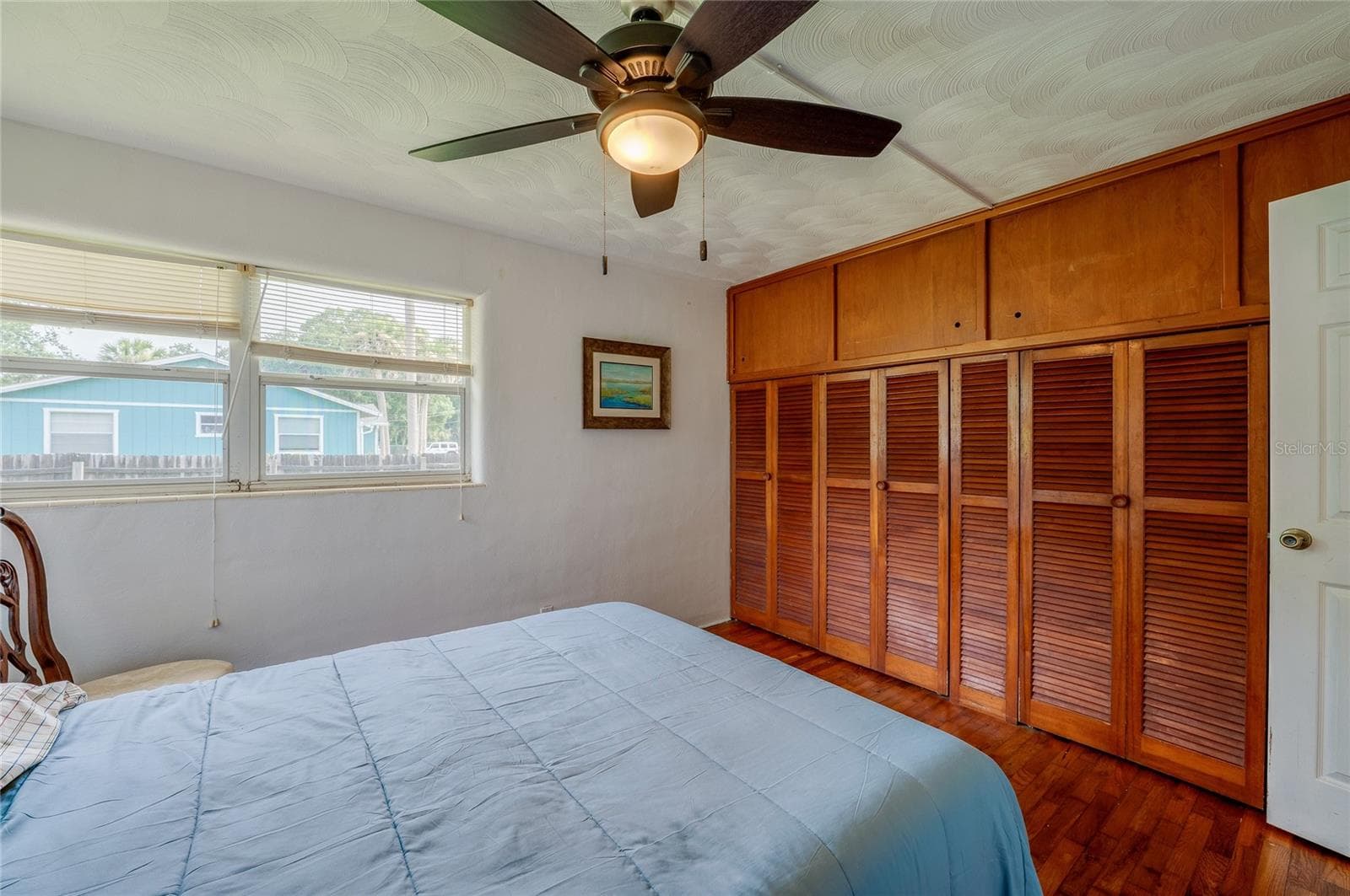 Bright bedroom featuring an expansive wall of built-in closet space, hardwood flooring, and a ceiling fan. Windows provide abundant illumination and framed views of the surrounding outdoors. - 1101 16TH ST, EDGEWATER