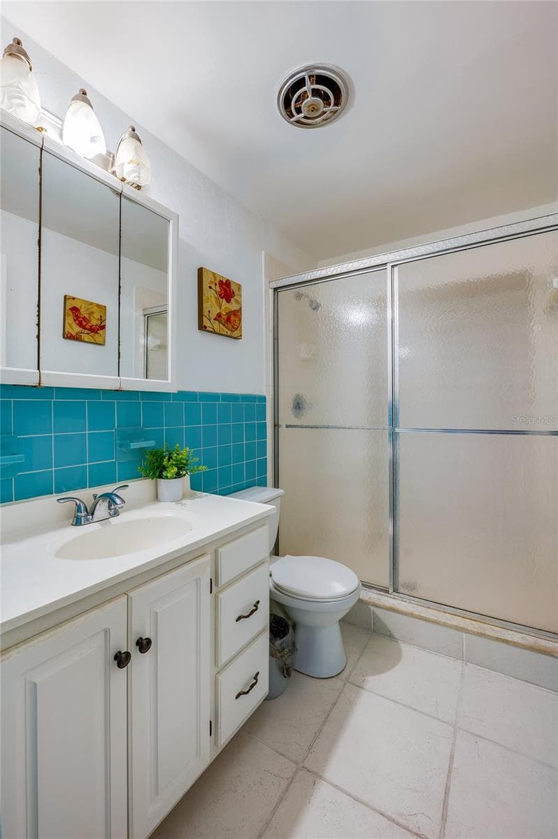 Classic bathroom showcasing vibrant turquoise wall tile accents, a white vanity with built-in storage, and a sliding glass shower enclosure. Bright vanity lighting and neutral floor tiles complete the clean design. - 1101 16TH ST, EDGEWATER