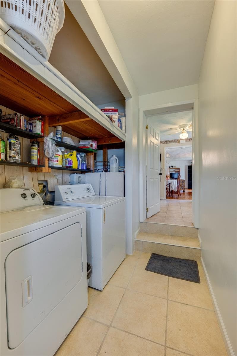 Dedicated utility room equipped with full-sized washer and dryer units, overhead wooden shelving, and a short step-up leading to adjacent living areas. - 1101 16TH ST, EDGEWATER