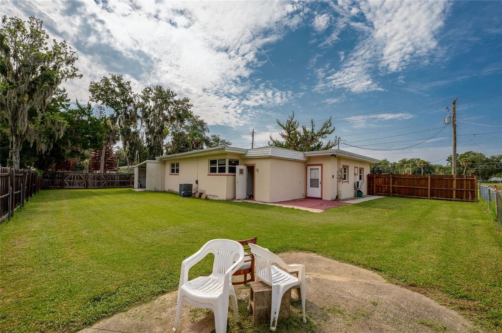 Broad rear view of the single-story home featuring a fully fenced grassy lawn under a vast sky with scattered clouds. - 1101 16TH ST, EDGEWATER