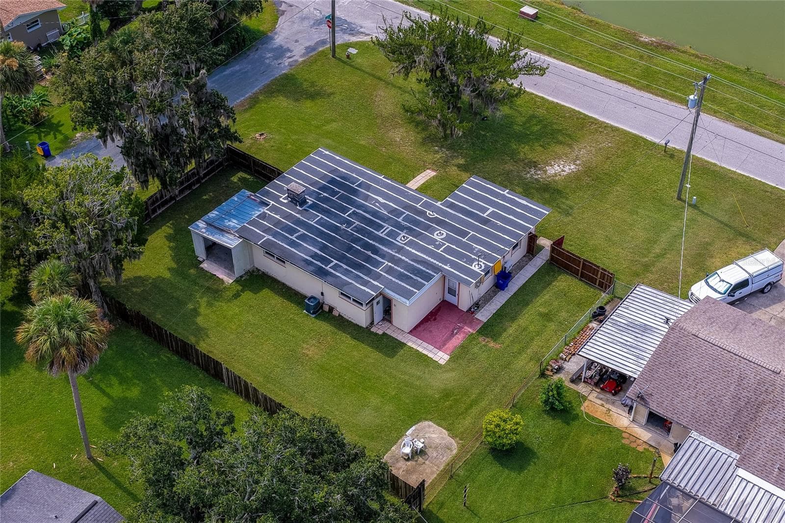 Elevated aerial perspective showcasing the home's dark roof, attached storage shelter, and fully fenced green backyard. The surrounding lot offers privacy with mature trees and proximity to quiet residential streets. - 1101 16TH ST, EDGEWATER