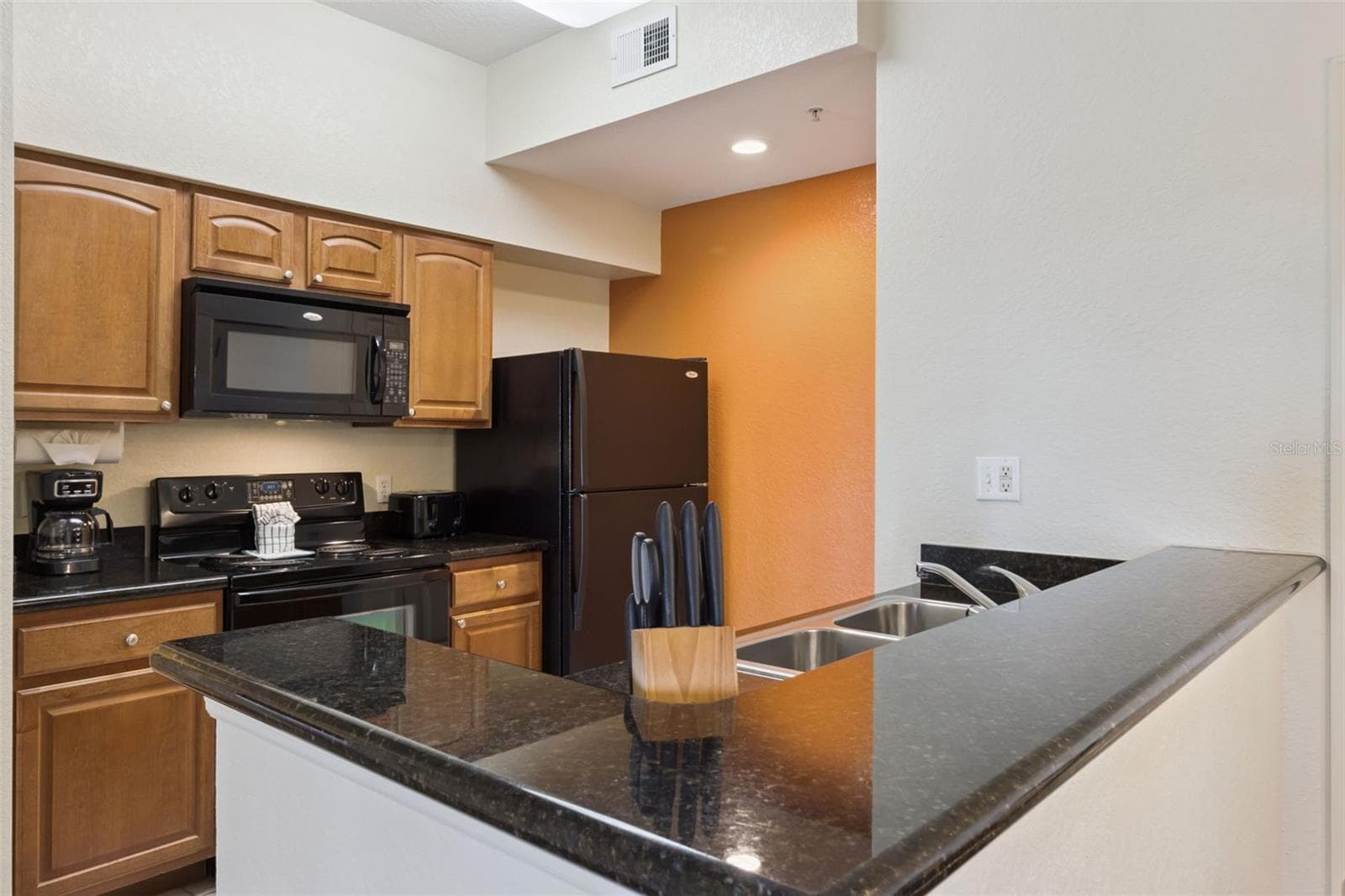 Kitchen | Wood cabinetry, dark granite countertops, and coordinated appliances create a functional cooking space. - 8101 RESORT VILLAGE DR #31110, ORLANDO