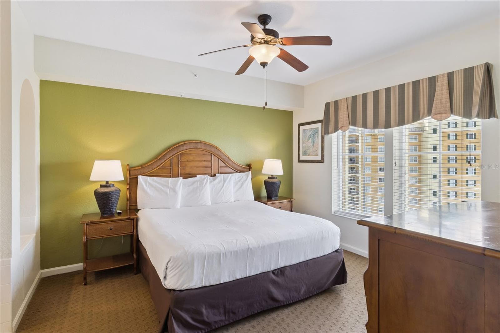 Primary Bedroom | A spacious bedroom features an accent wall, ceiling fan, and windows overlooking resort. - 8101 RESORT VILLAGE DR #31110, ORLANDO