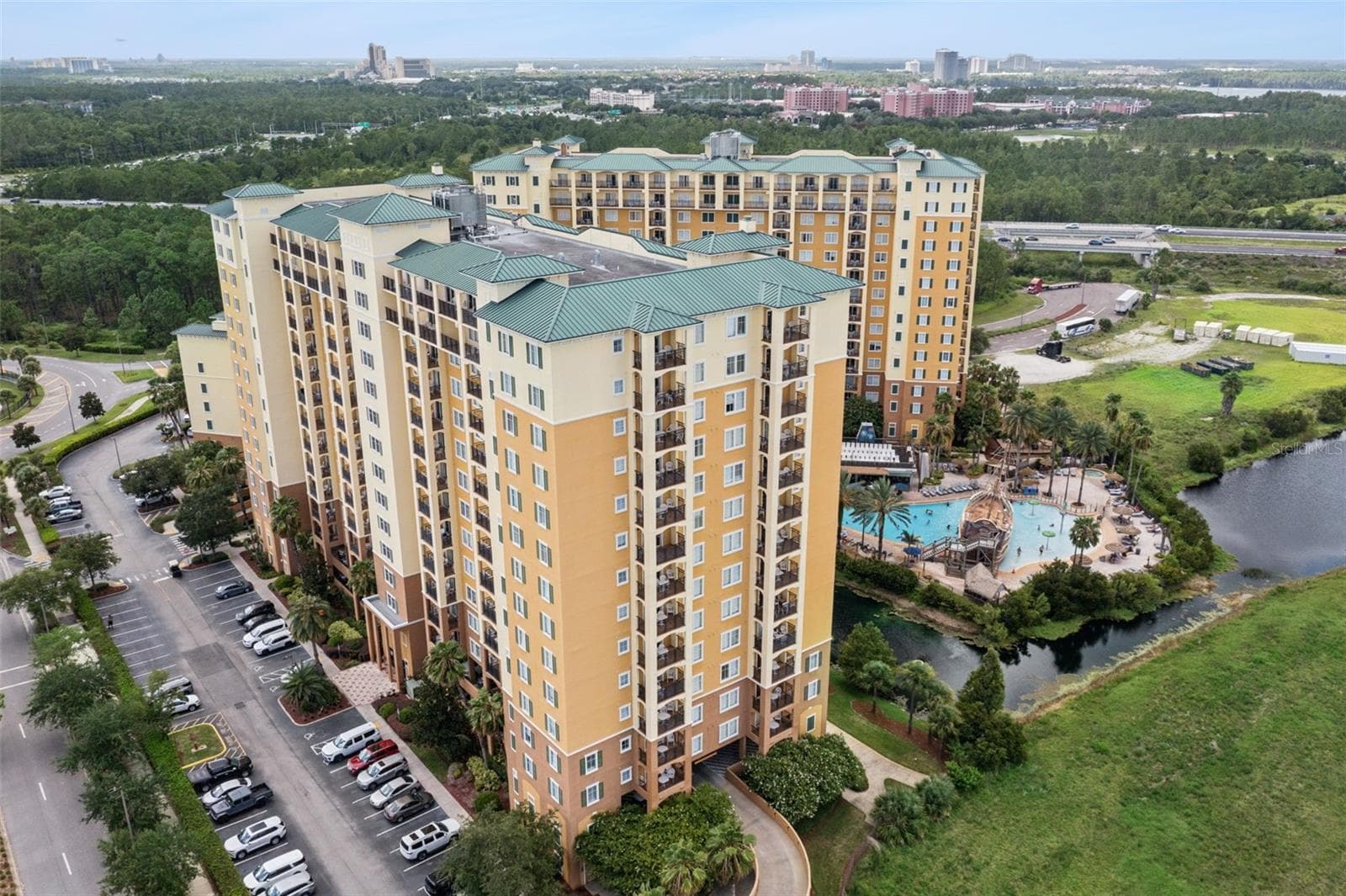 Resort Exterior | An aerial view captures the high-rise buildings, pool complex, pond, parking areas, and surrounding landscape. - 8101 RESORT VILLAGE DR #31110, ORLANDO