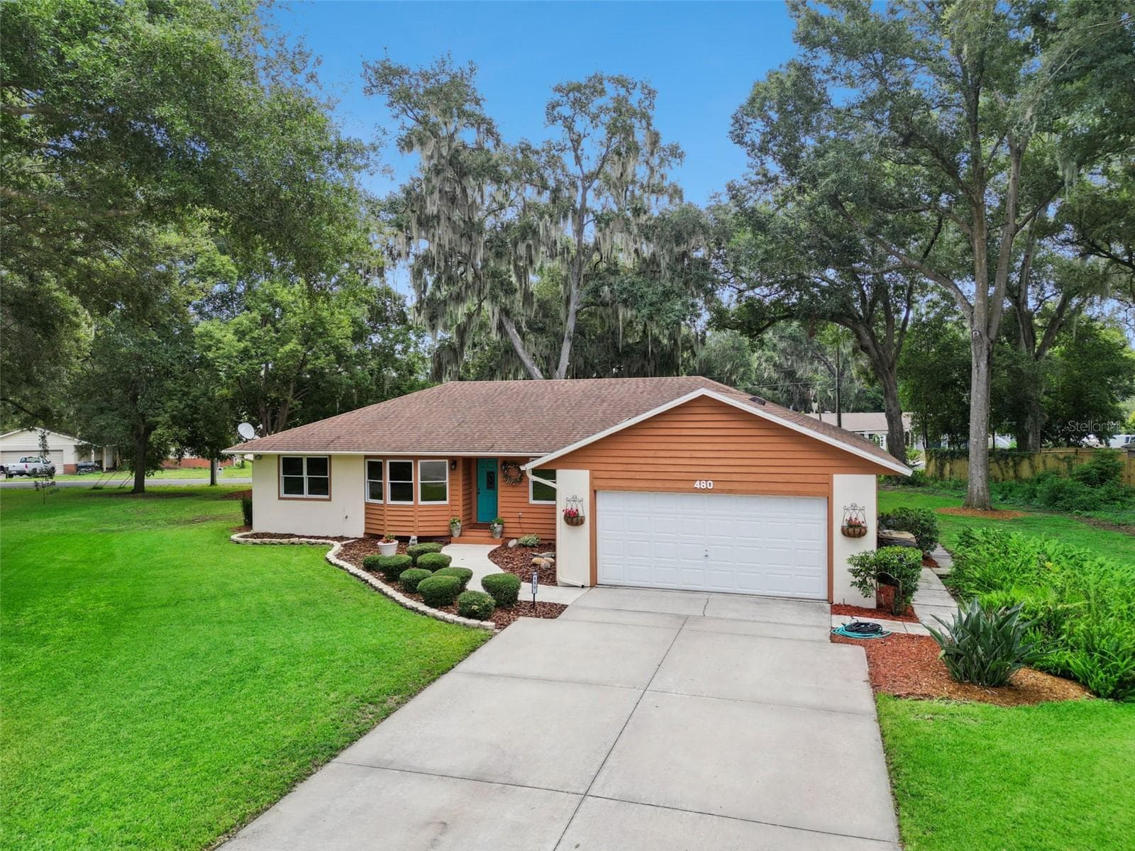 Wide curb appeal view of 480 Lake Forest Cir showing the expansive front yard, mature live oaks with Spanish moss, and well-maintained exterior in Mount Dora, FL - 480 LAKE FOREST CIR, MOUNT DORA