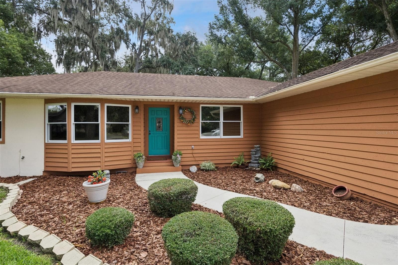 Inviting front entry with teal door, leaded glass inset, coach lanterns, and low-maintenance mulch landscaping at this Mount Dora home listed at $380,900 - 480 LAKE FOREST CIR, MOUNT DORA