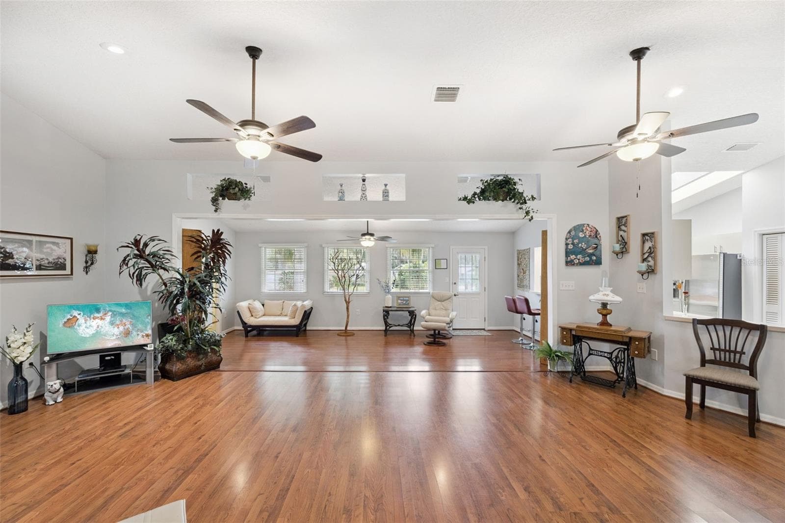 Expansive great room with multiple ceiling fans, decorative plant shelves, and laminate floors flowing through 1,909 sq ft of open living space in this split-plan home - 480 LAKE FOREST CIR, MOUNT DORA
