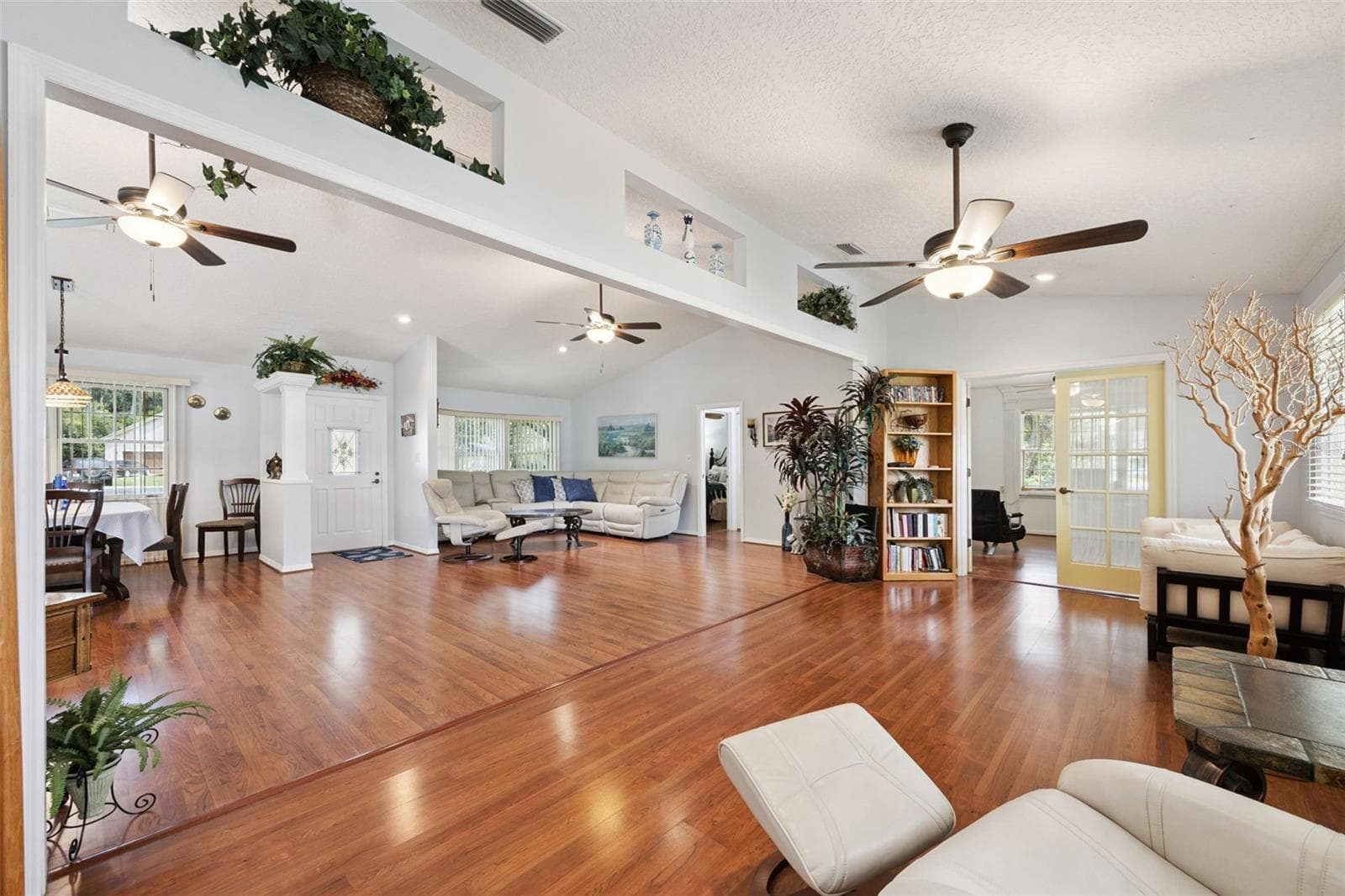 Panoramic view showing the living room, dining area, foyer, and French door bonus room connected by vaulted ceilings and continuous laminate floors at 480 Lake Forest Cir - 480 LAKE FOREST CIR, MOUNT DORA