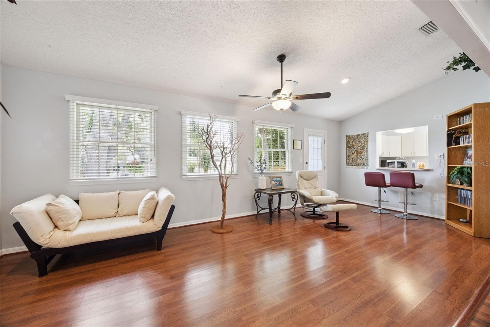 Family room (23x10) with ceiling fan, multiple windows overlooking the backyard, and bar seating at the kitchen pass-through in this Mount Dora split-plan home - 480 LAKE FOREST CIR, MOUNT DORA
