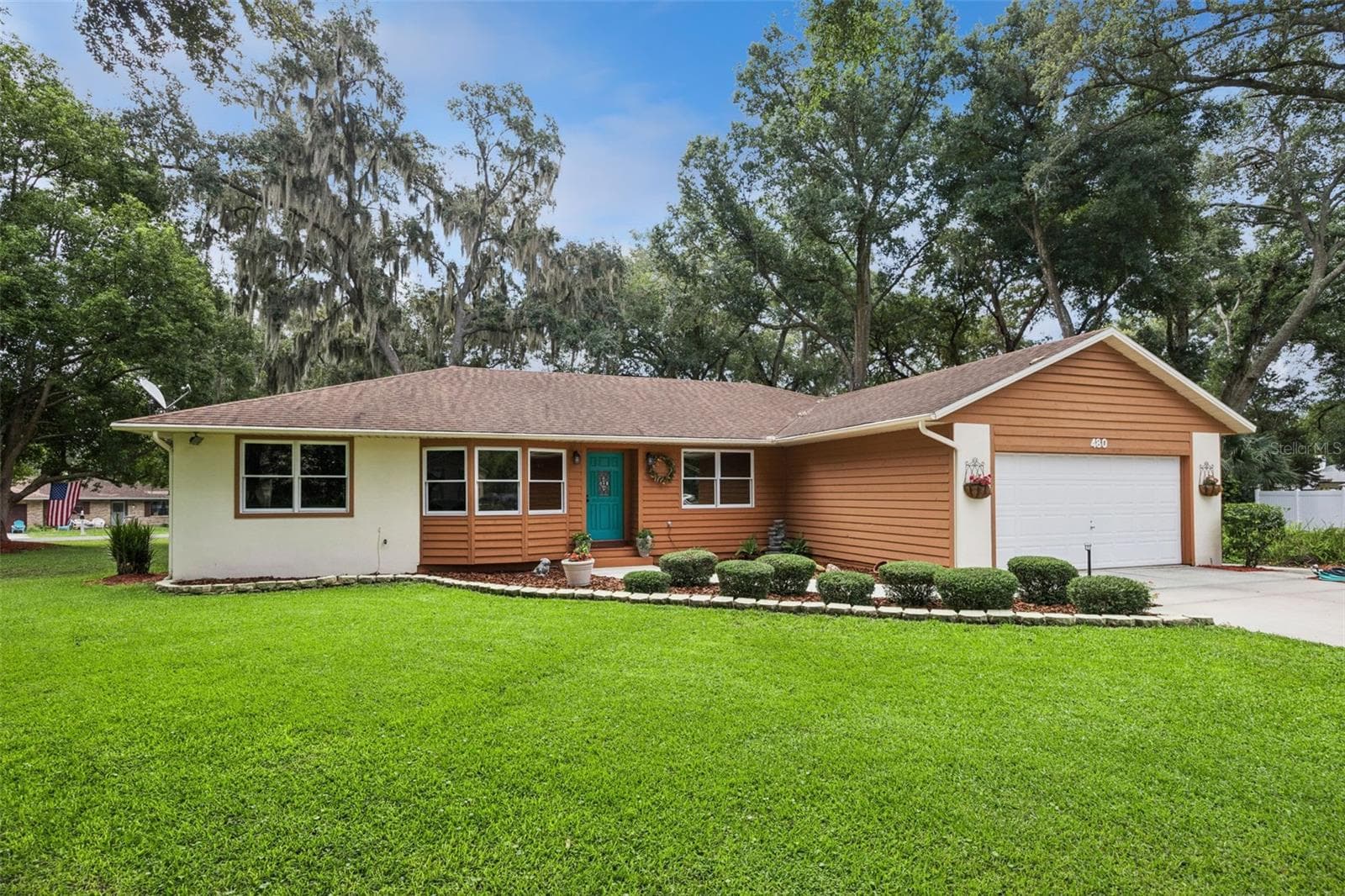 Front exterior showing the stucco and cedar siding, stone-bordered landscape beds, and mature lawn at this 1987-built Mount Dora home - 480 LAKE FOREST CIR, MOUNT DORA