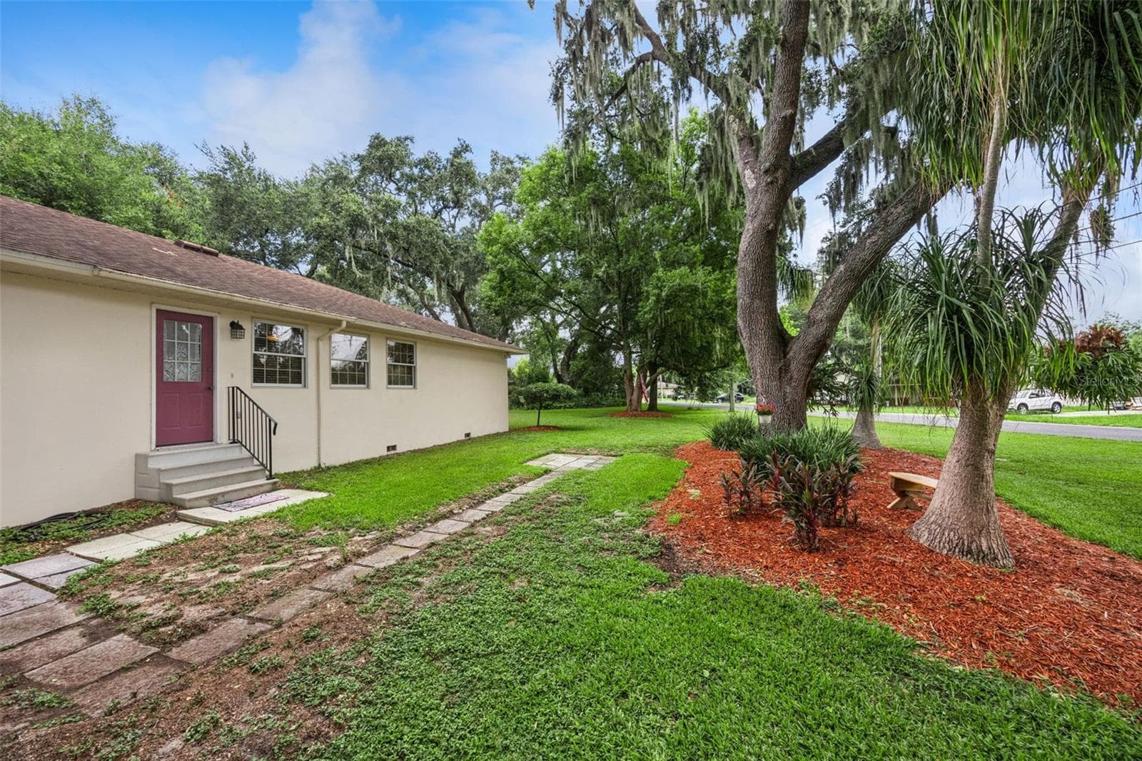 Side yard with red mulch beds, mature trees, and American flag at 480 Lake Forest Cir in Lake Forest, Mount Dora - 480 LAKE FOREST CIR, MOUNT DORA