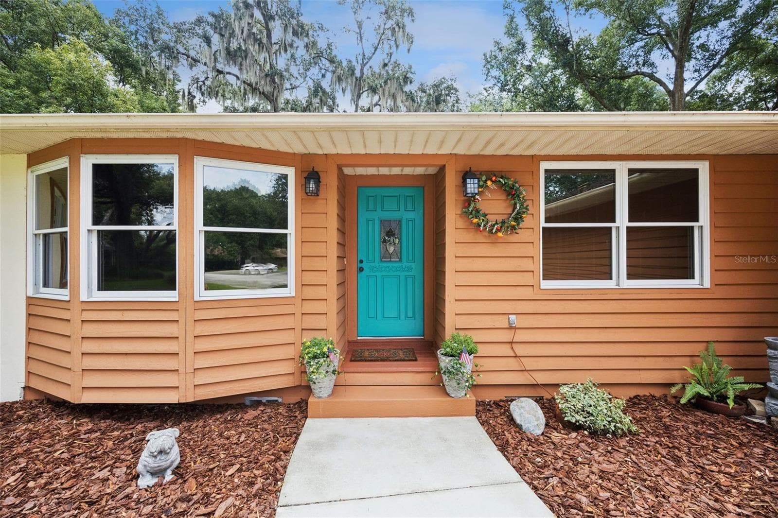Welcoming front door detail with decorative leaded glass inset, bay window, coach lanterns, and potted plants at 480 Lake Forest Cir, a move-in ready home in Mount Dora's Lake Forest community - 480 LAKE FOREST CIR, MOUNT DORA