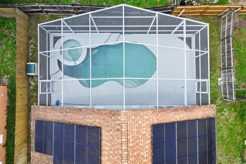 Aerial view of the screen-enclosed pool, spa, and solar panels. - 97 ABBEY HOLLOW DR, APOPKA