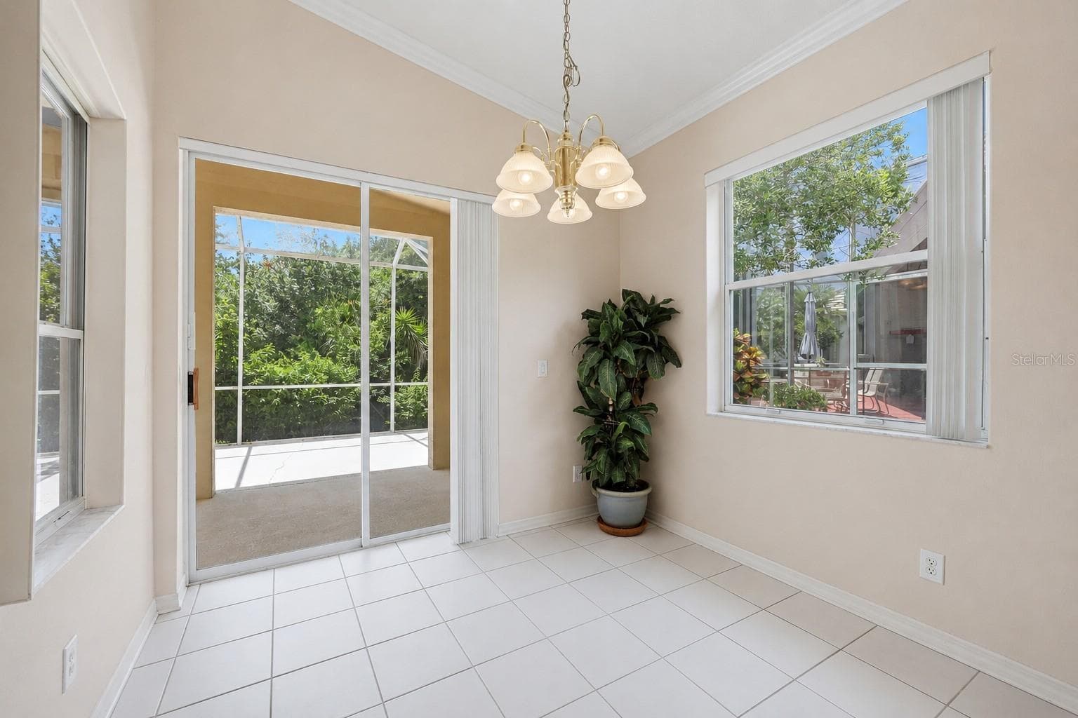 Light-filled dining area with chandelier and sliding glass doors opening to screened lanai - 8492 IDLEWOOD CT, LAKEWOOD RANCH