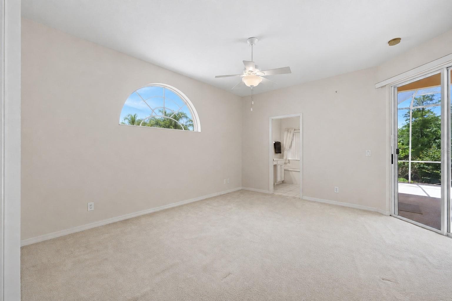 Primary bedroom with ceiling fan, neutral Bright flexible living space with arched window, ceiling fan and access to outdoor living area - 8492 IDLEWOOD CT, LAKEWOOD RANCH