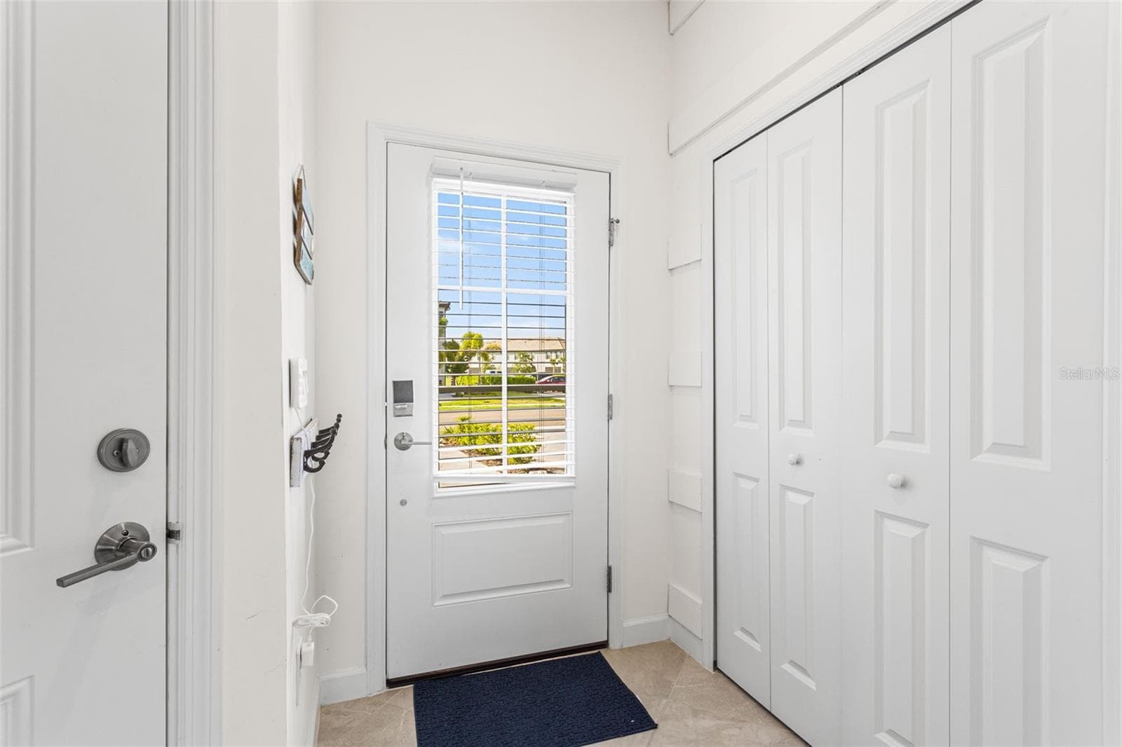 Step through a decorative front door with glass insert, equipped with a keyless entry pad and security camera, into a welcoming foyer featuring a coastal-inspired half bath and convenient storage - 14275 PINE LODGE LN, FORT MYERS