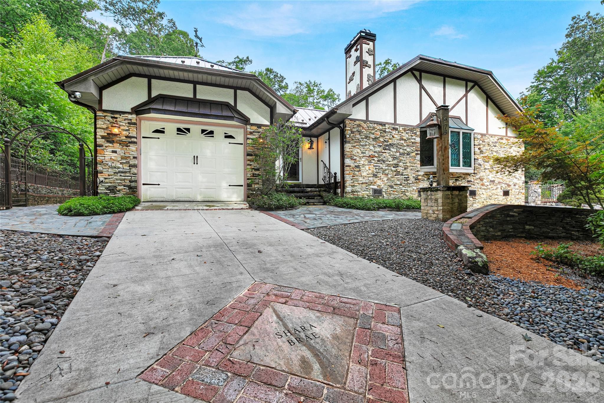Single car garage and driveway on far-left end of the house. Easy In - Easy Out.! Notice the custom chimney above the metal roof, and the iron entry gate to the left. - 275 Hubbard Hollow Road, Rosman