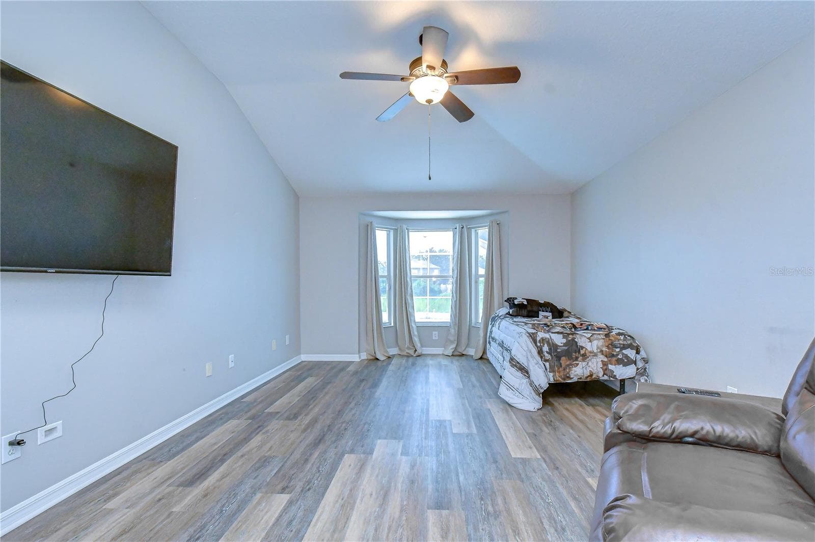 Spacious living area featuring low-maintenance wood-look flooring, ceiling fan, wall-mounted TV setup, and abundant natural light through glass doors. - 11117 RODEO LN, RIVERVIEW