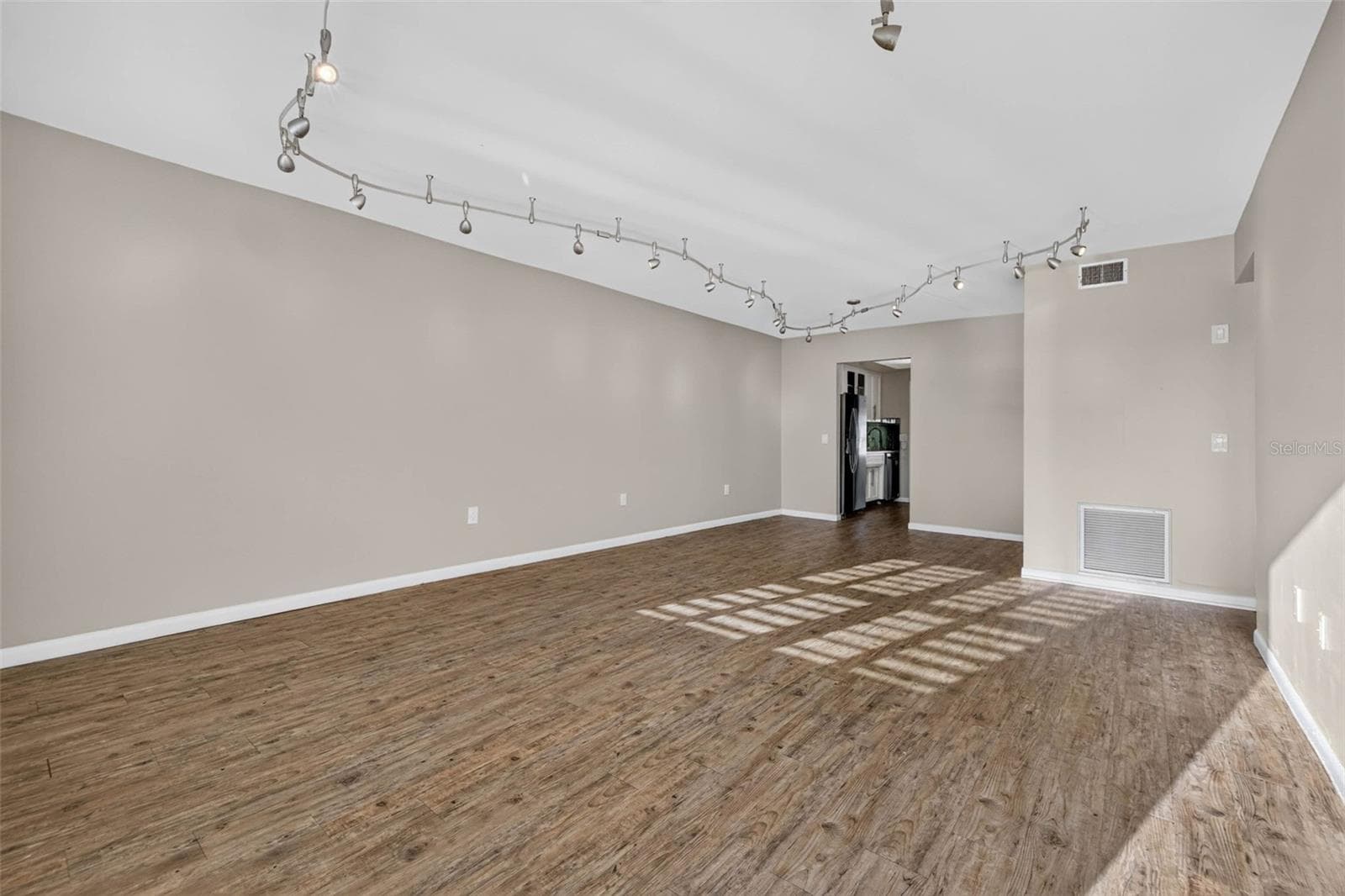 This spacious living room offers an open, versatile layout with abundant natural light, stylish contemporary track lighting, and durable wood-look luxury vinyl flooring throughout - 6015 19TH ST N #215, ST PETERSBURG