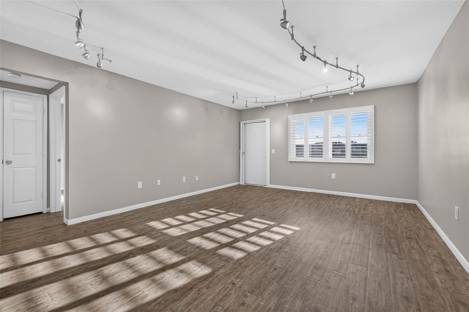 Bright, spacious living room featuring luxury vinyl flooring, plantation shutters, modern track lighting, and an open layout perfect for everyday living and entertaining. - 6015 19TH ST N #215, ST PETERSBURG