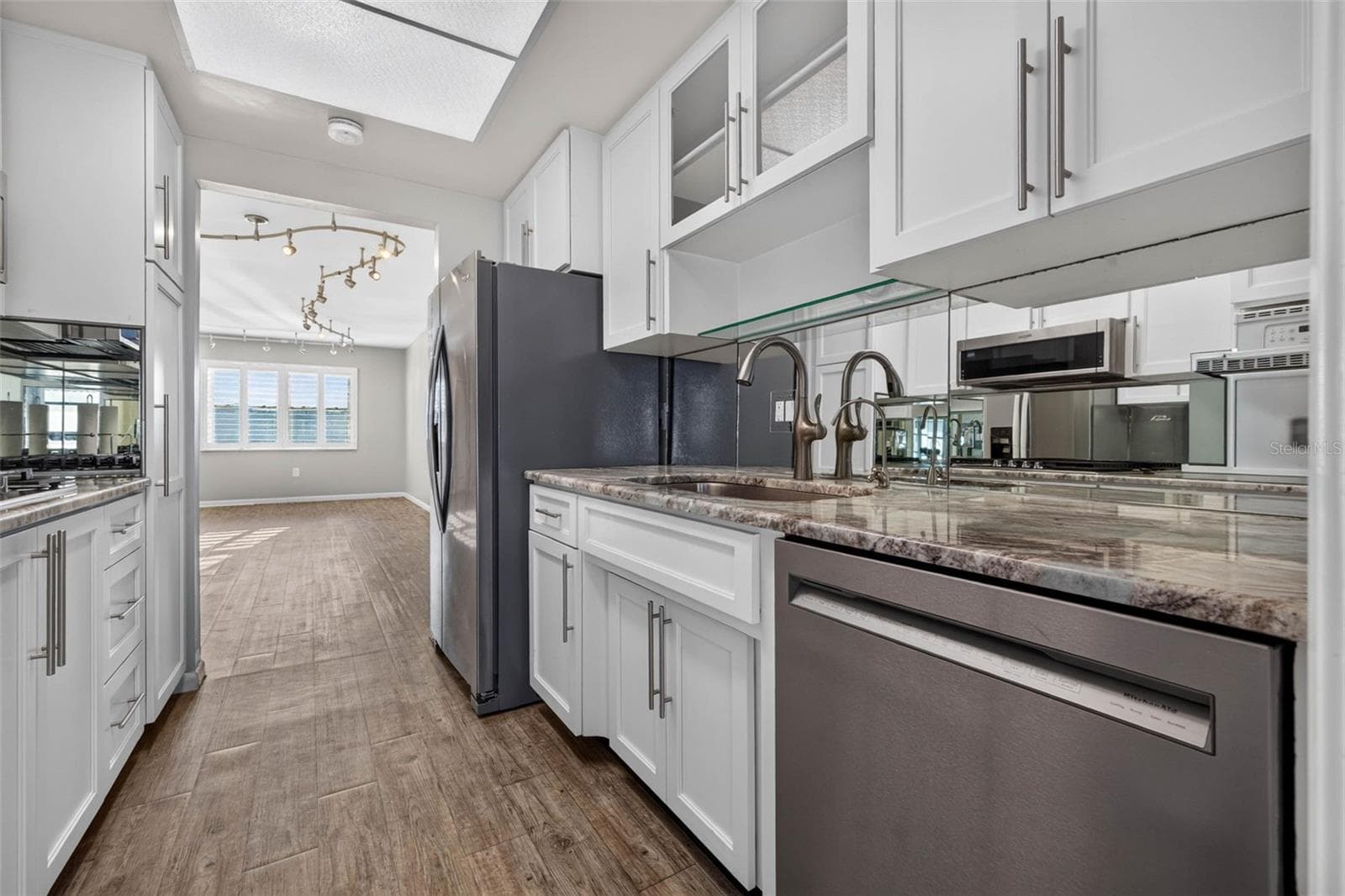 Updated galley kitchen featuring white shaker cabinets, stainless steel appliances, ample counter space, and a bright, open flow to the dining and living areas. - 6015 19TH ST N #215, ST PETERSBURG