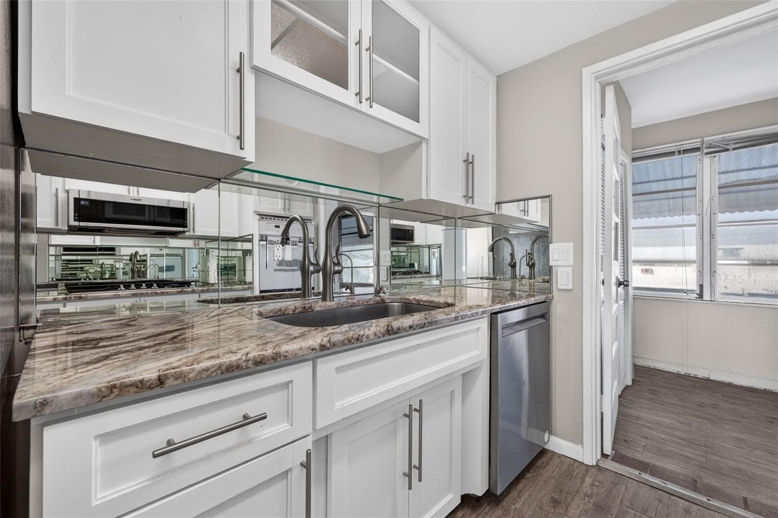 Kitchen with white shaker cabinets, mirrored backsplash, stainless steel appliances, abundant counter space, and modern finishes. - 6015 19TH ST N #215, ST PETERSBURG