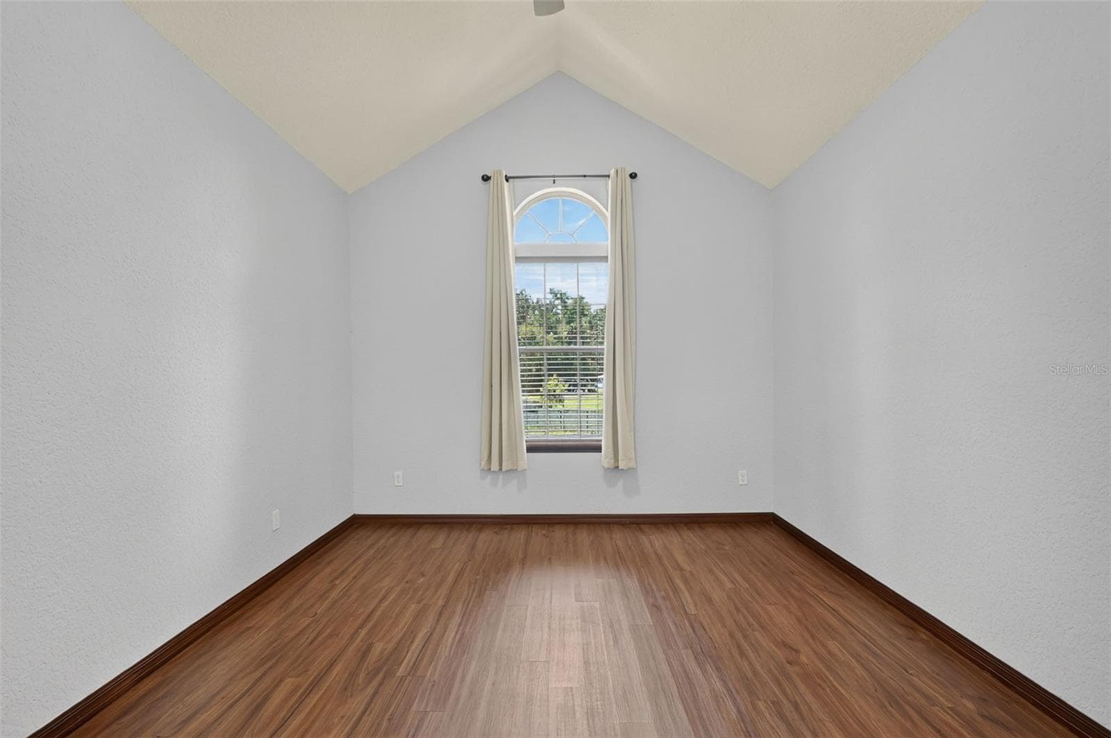 A charming upstairs bedroom features a stunning arched window, vaulted ceilings, and beautiful hardwood floors flooded with natural light. - 4617 ROUND LAKE RD, APOPKA