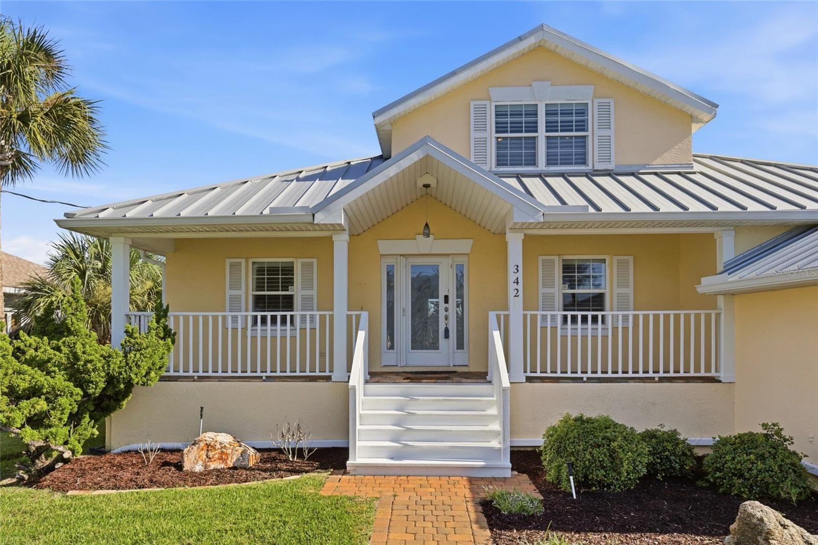 Front exterior — Front elevation with standing-seam metal roof, covered porch, painted railings, and paver walkway leading to the entry. - 342 N 12TH ST, FLAGLER BEACH