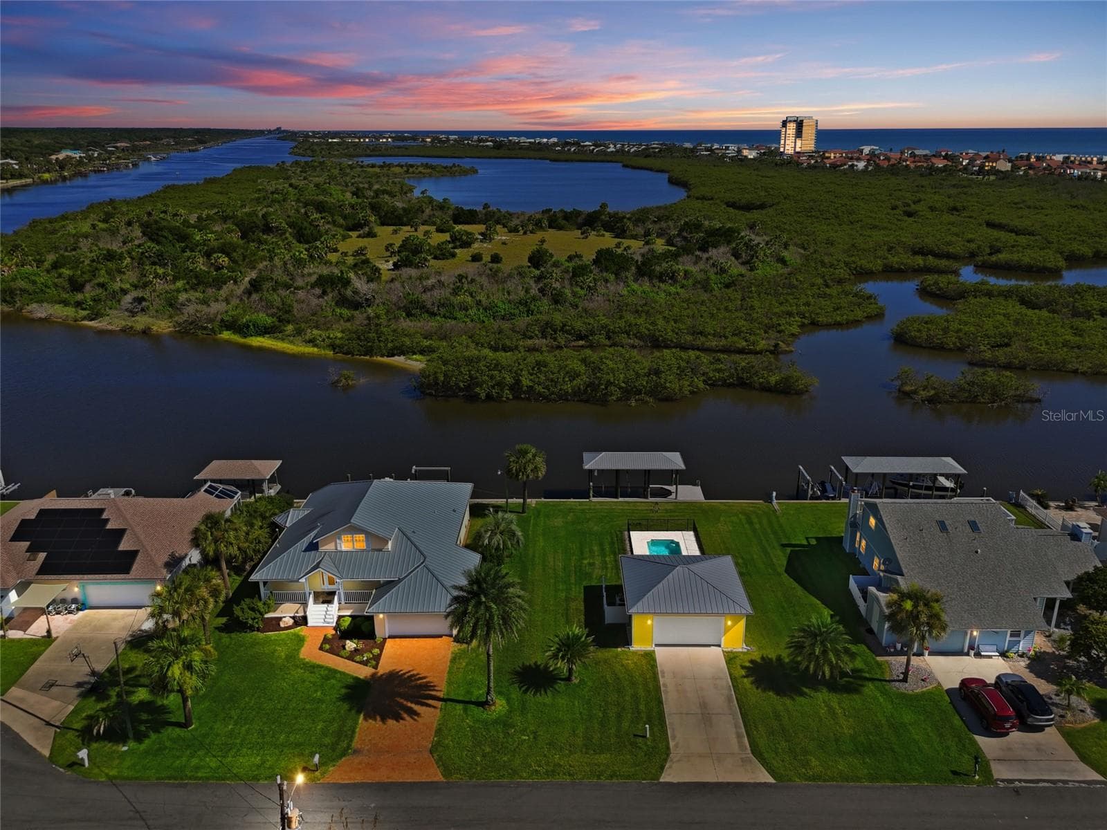 Aerial view (dusk) — Twilight aerial view of the canal-front home highlighting the dock with two covered boat lifts, backyard pool, and unobstructed water access to the Intracoastal Waterway. - 342 N 12TH ST, FLAGLER BEACH