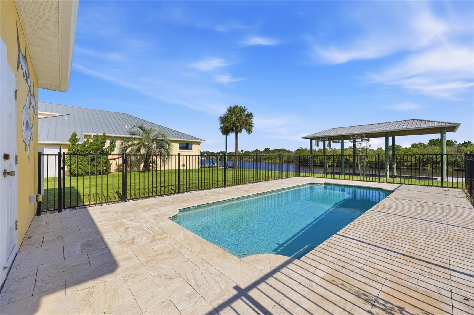 Pool area — Fenced backyard pool with paver deck, canal views, and a covered dock structure visible beyond the fence line. - 342 N 12TH ST, FLAGLER BEACH