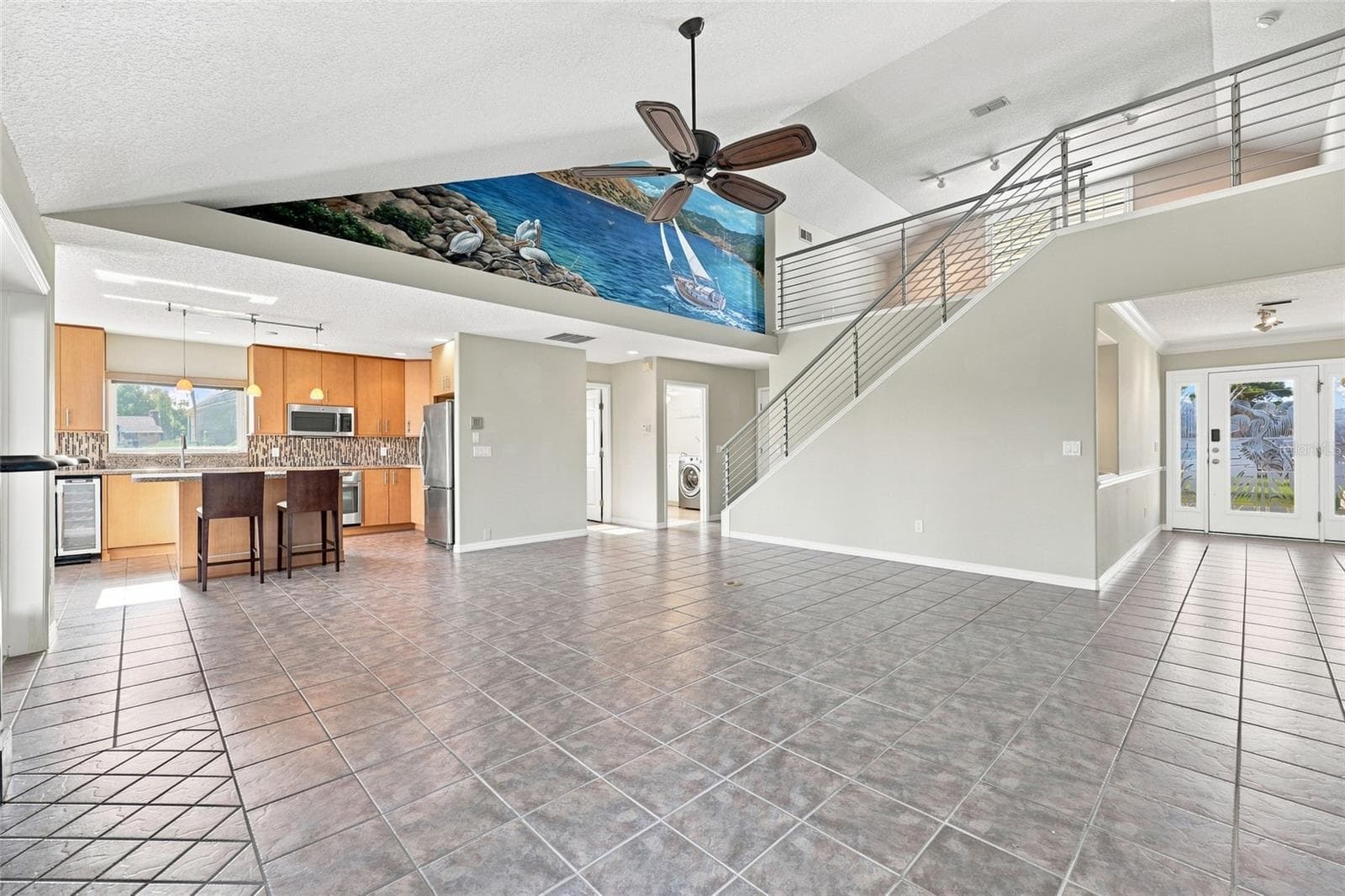 Great room — Open-concept great room with tile flooring, custom hand-painted coastal mural along the vaulted ceiling, staircase with cable railing, and kitchen visible beyond. - 342 N 12TH ST, FLAGLER BEACH