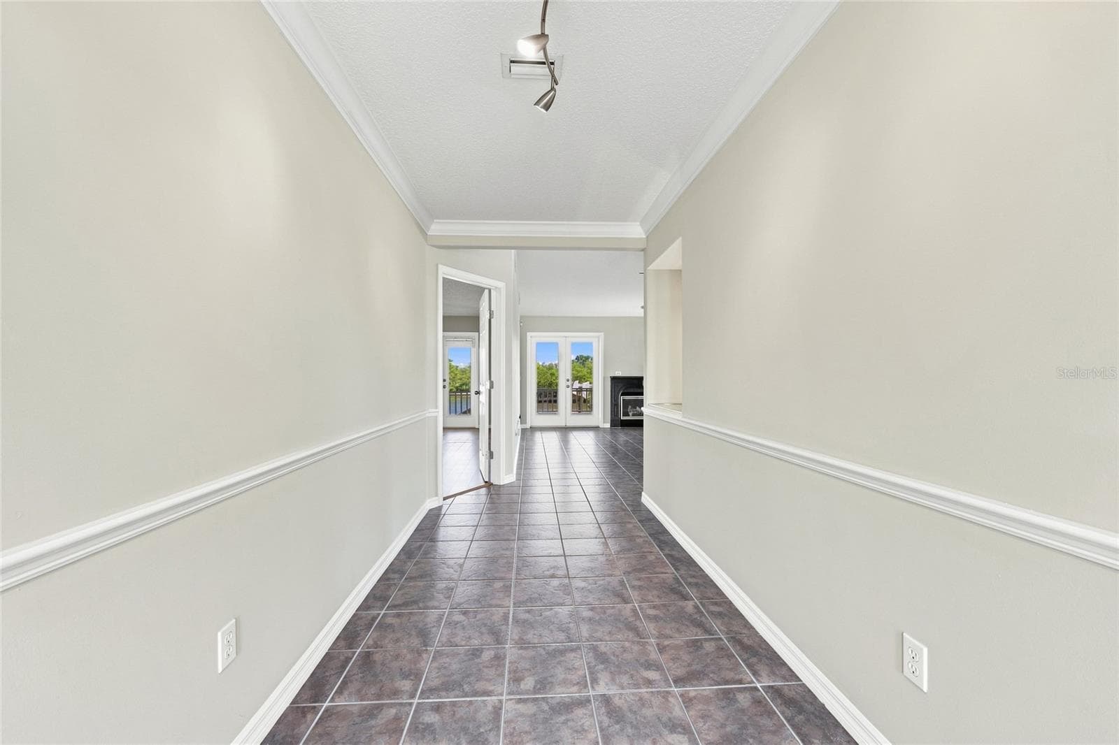 Interior hallway — Tiled hallway with crown molding and chair rail leading toward the living area, with French doors opening to a water-view balcony visible ahead. - 342 N 12TH ST, FLAGLER BEACH