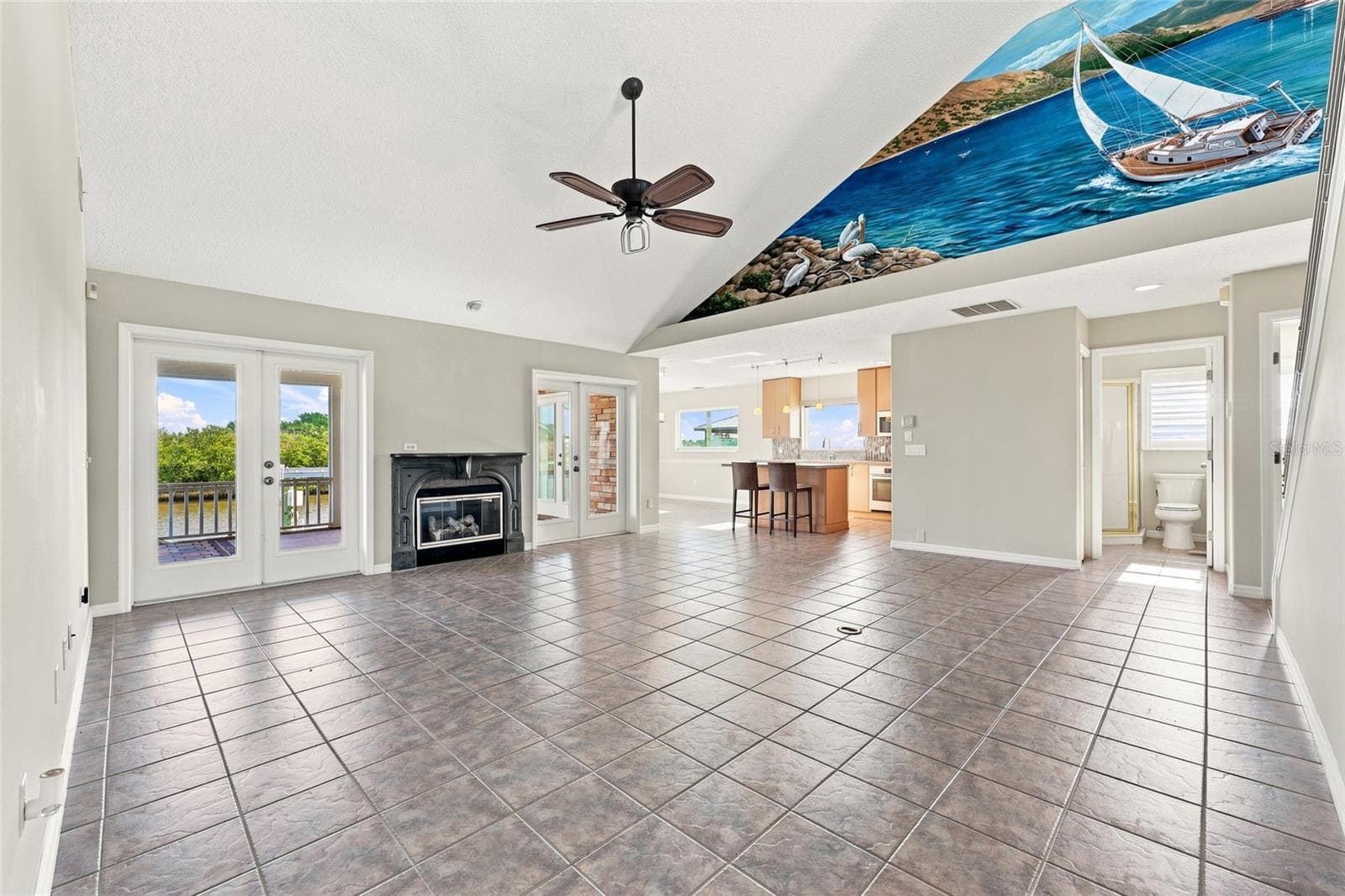 Great room — Vaulted great room with gas fireplace, French doors to a canal-view balcony, tile flooring, and an open sightline to the kitchen and staircase. - 342 N 12TH ST, FLAGLER BEACH