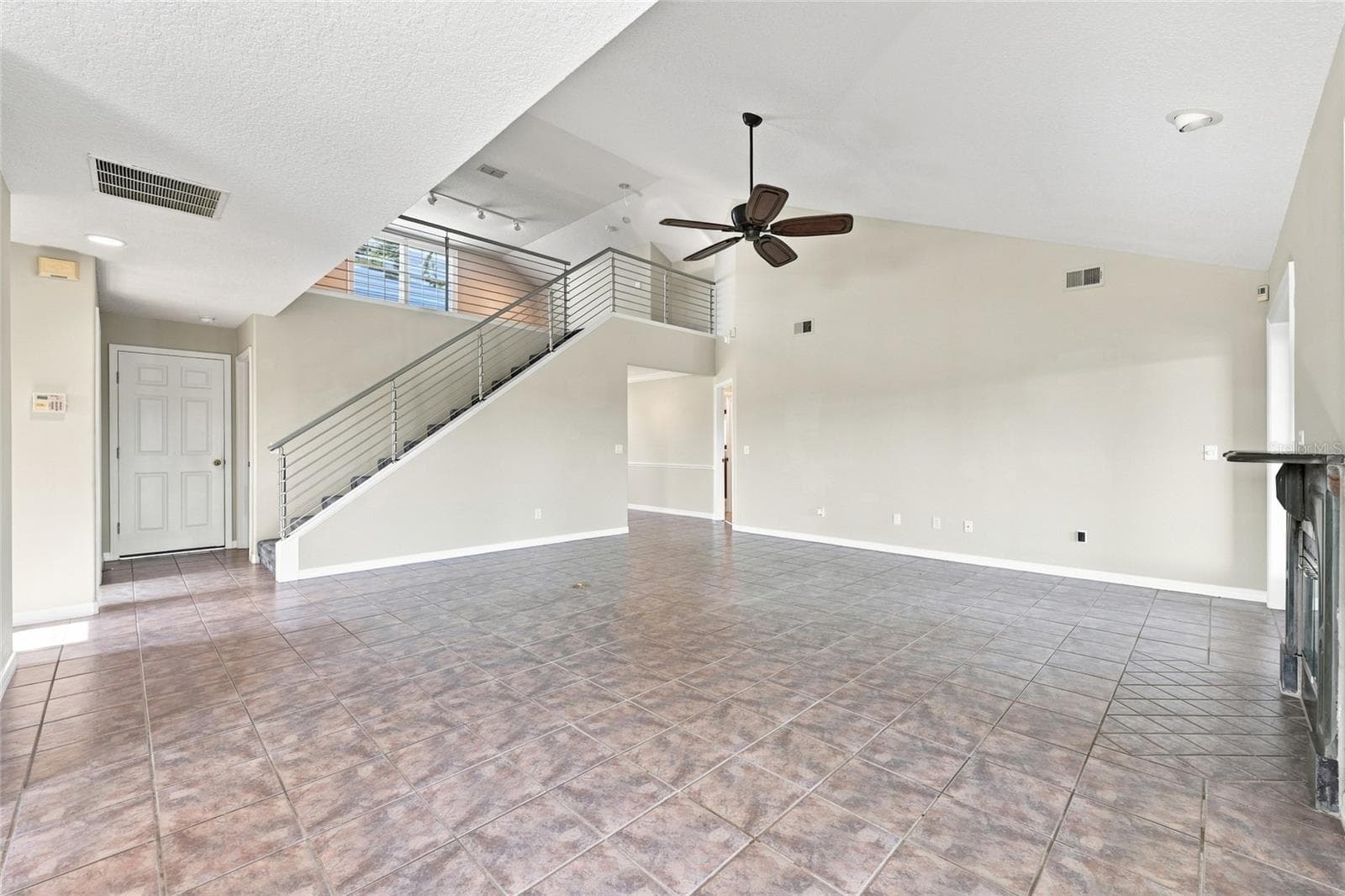 Living area — Open living space with tile flooring, staircase with cable railing to the loft, and natural light from the front entry doors. - 342 N 12TH ST, FLAGLER BEACH