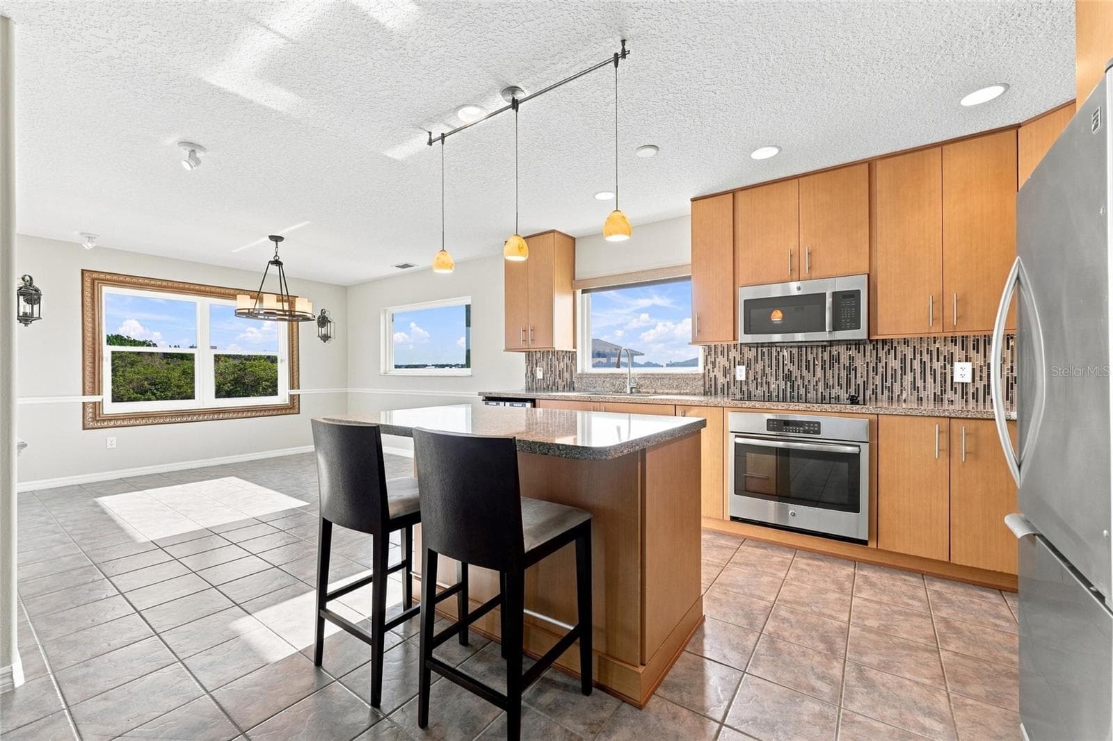 Kitchen — Renovated kitchen with granite island seating two, pendant lighting, glass tile backsplash, and stainless steel appliances with a canal view through the window. - 342 N 12TH ST, FLAGLER BEACH