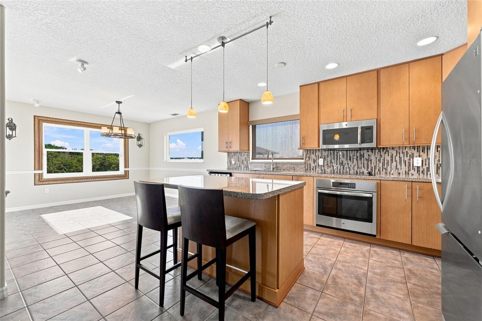 Kitchen — Renovated kitchen showing granite island, stainless microwave and wall oven, and glass mosaic tile backsplash with natural light from multiple windows. - 342 N 12TH ST, FLAGLER BEACH