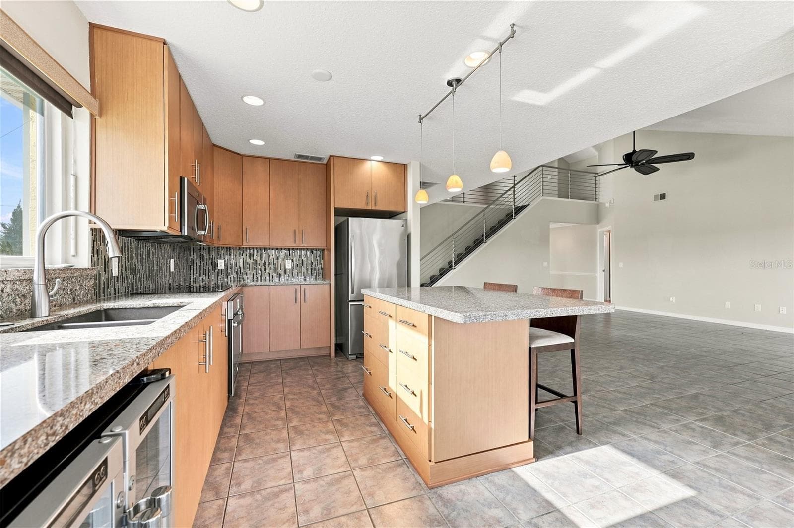 Kitchen — Kitchen view toward the staircase and open living area, with granite island, stainless refrigerator, and pendant lighting. - 342 N 12TH ST, FLAGLER BEACH