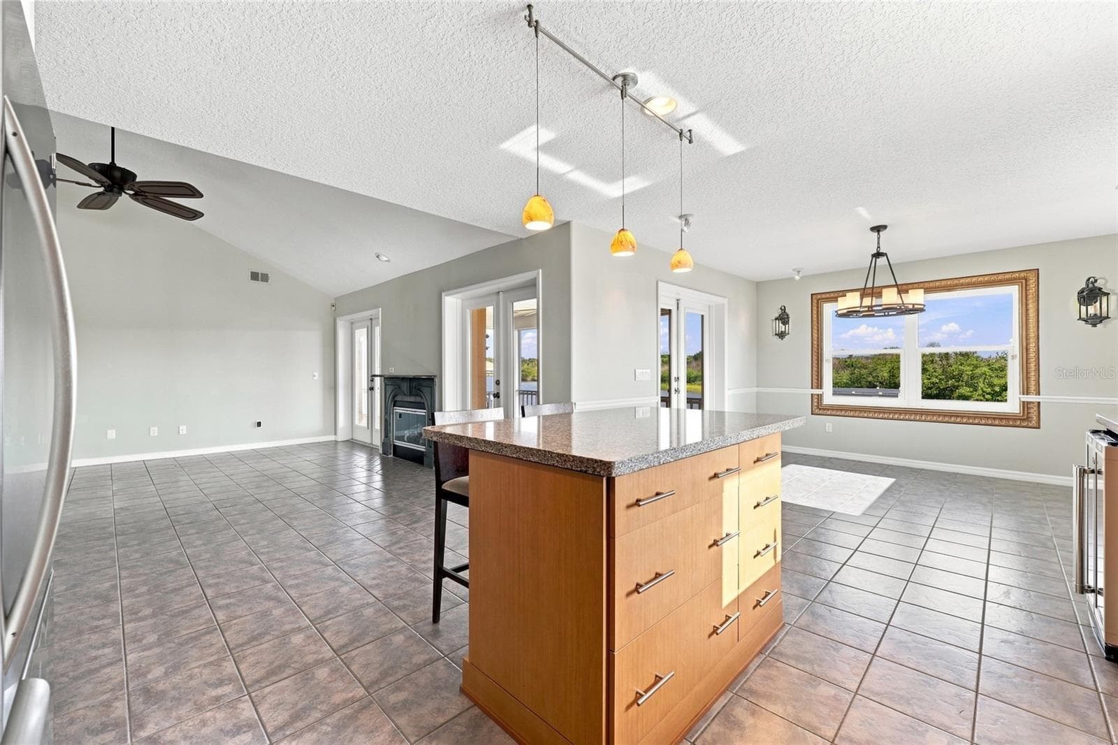 Kitchen and dining area — Open kitchen and breakfast area with granite island seating, chandelier, gas fireplace visible beyond, and framed picture window with canal views. - 342 N 12TH ST, FLAGLER BEACH