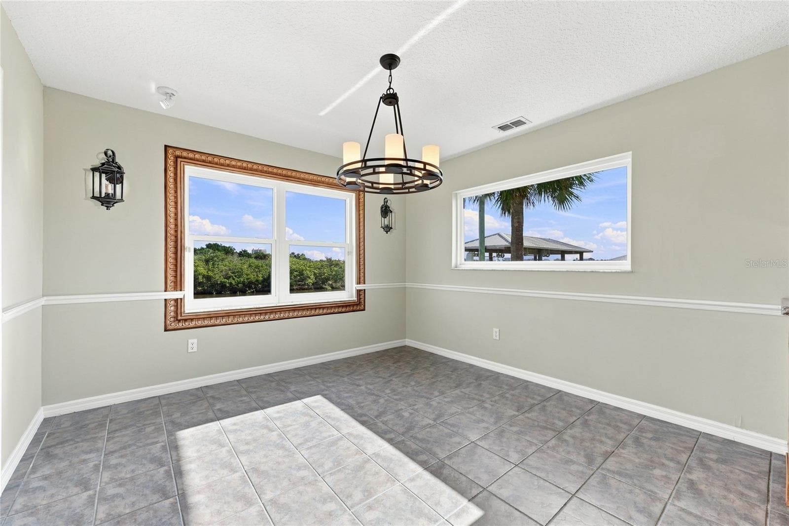 Breakfast nook — Breakfast nook with oversized picture-frame window overlooking the canal, second window with palm tree view, and wagon-wheel chandelier. - 342 N 12TH ST, FLAGLER BEACH