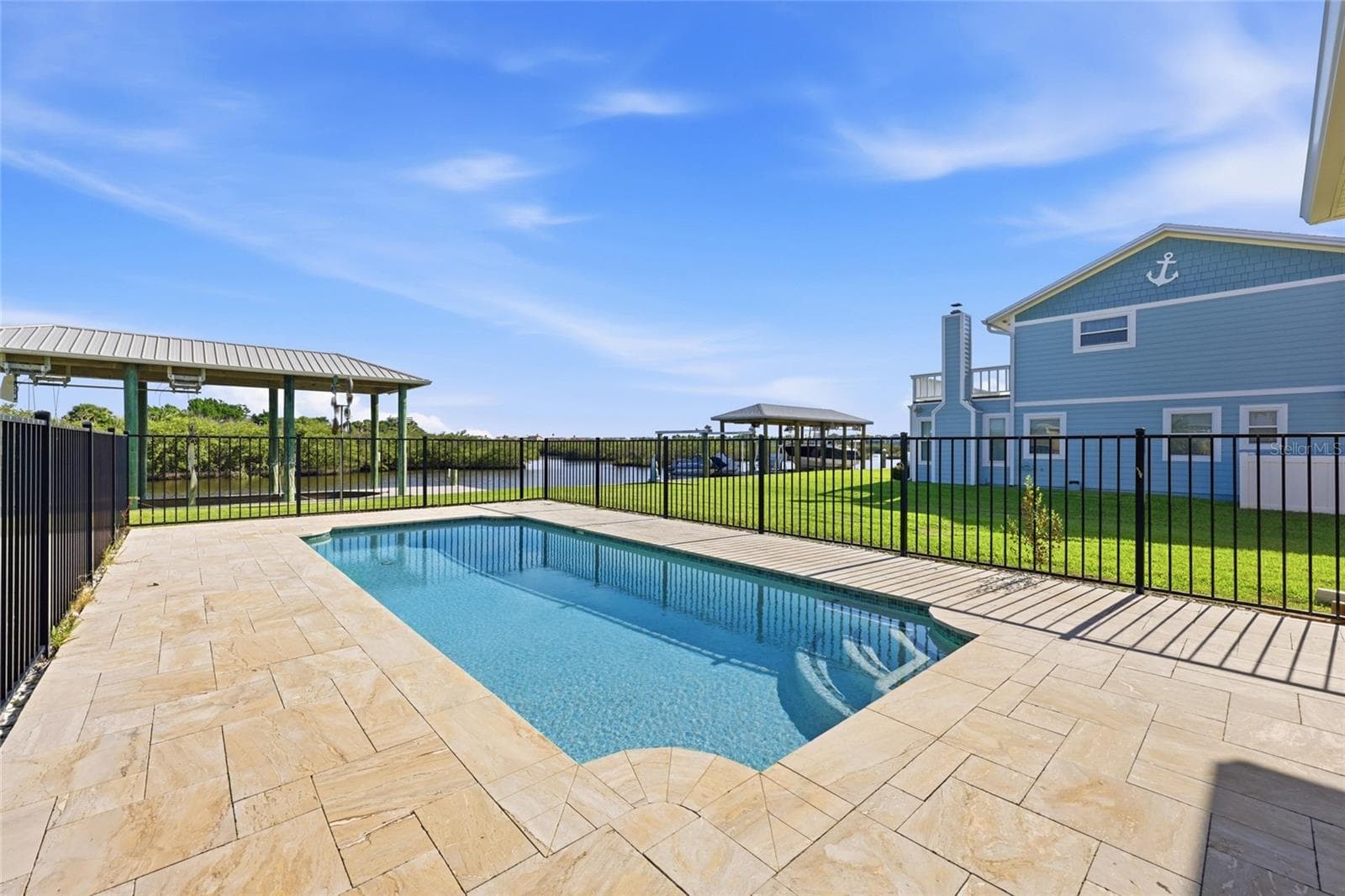 Pool and dock — Fenced pool with paver deck, covered boat lift structure, and canal frontage visible beyond the yard. - 342 N 12TH ST, FLAGLER BEACH