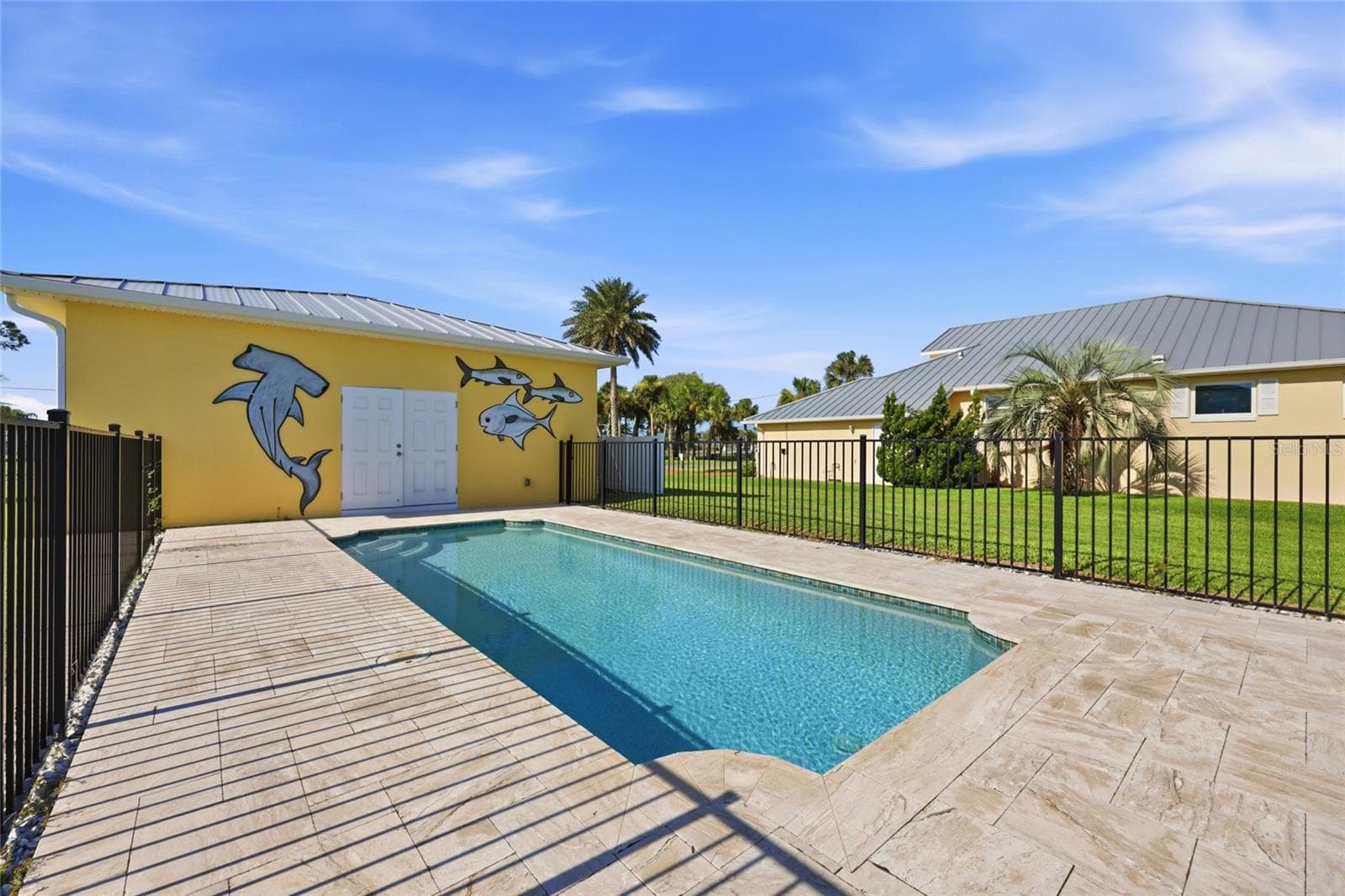 Pool with mural — Pool with paver deck bordered by a yellow poolside structure featuring a hand-painted hammerhead shark and fish mural. - 342 N 12TH ST, FLAGLER BEACH