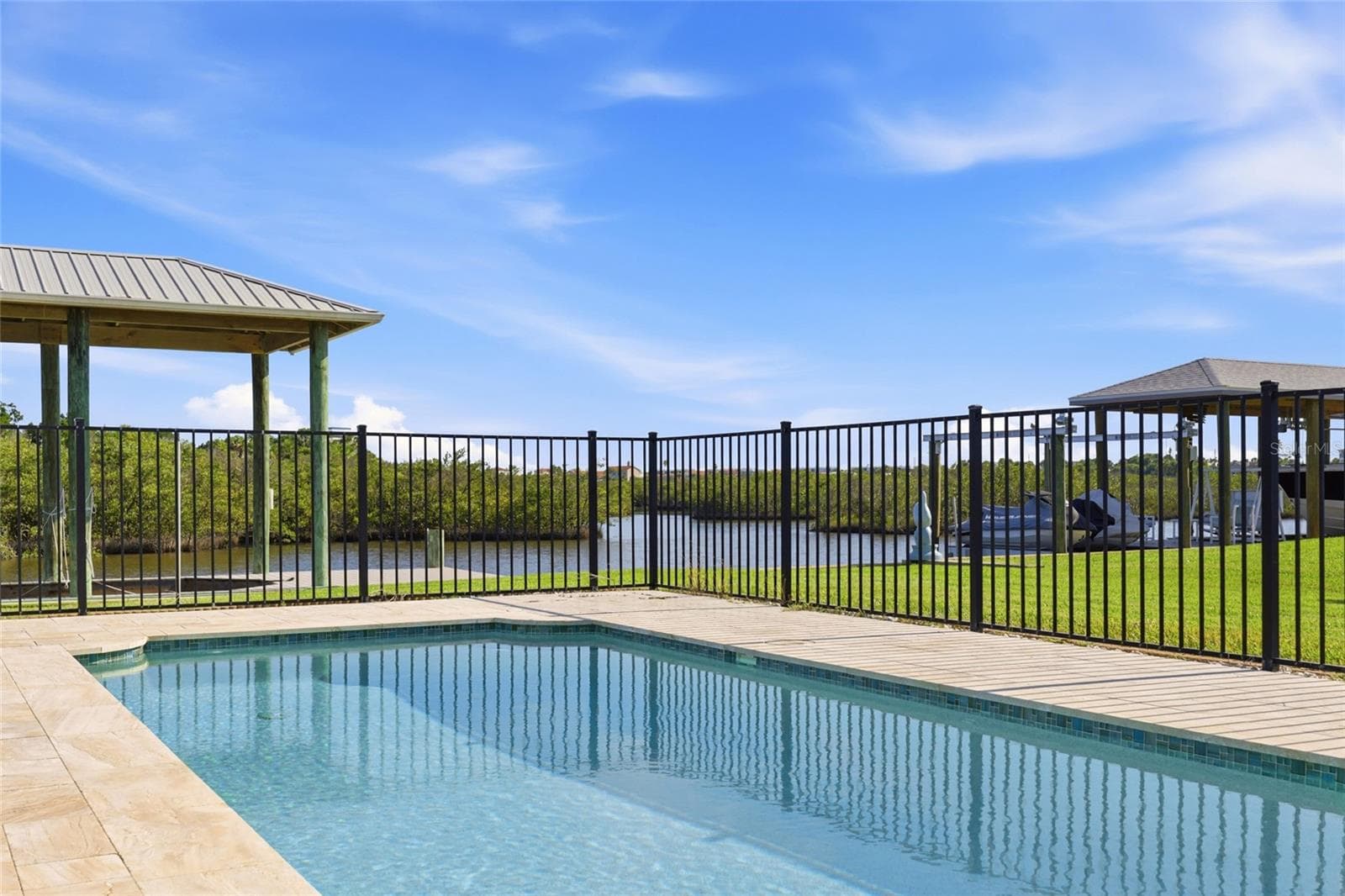 Pool corner — Corner view of the fenced pool with paver deck, canal and covered boat lift visible through the fence line. - 342 N 12TH ST, FLAGLER BEACH