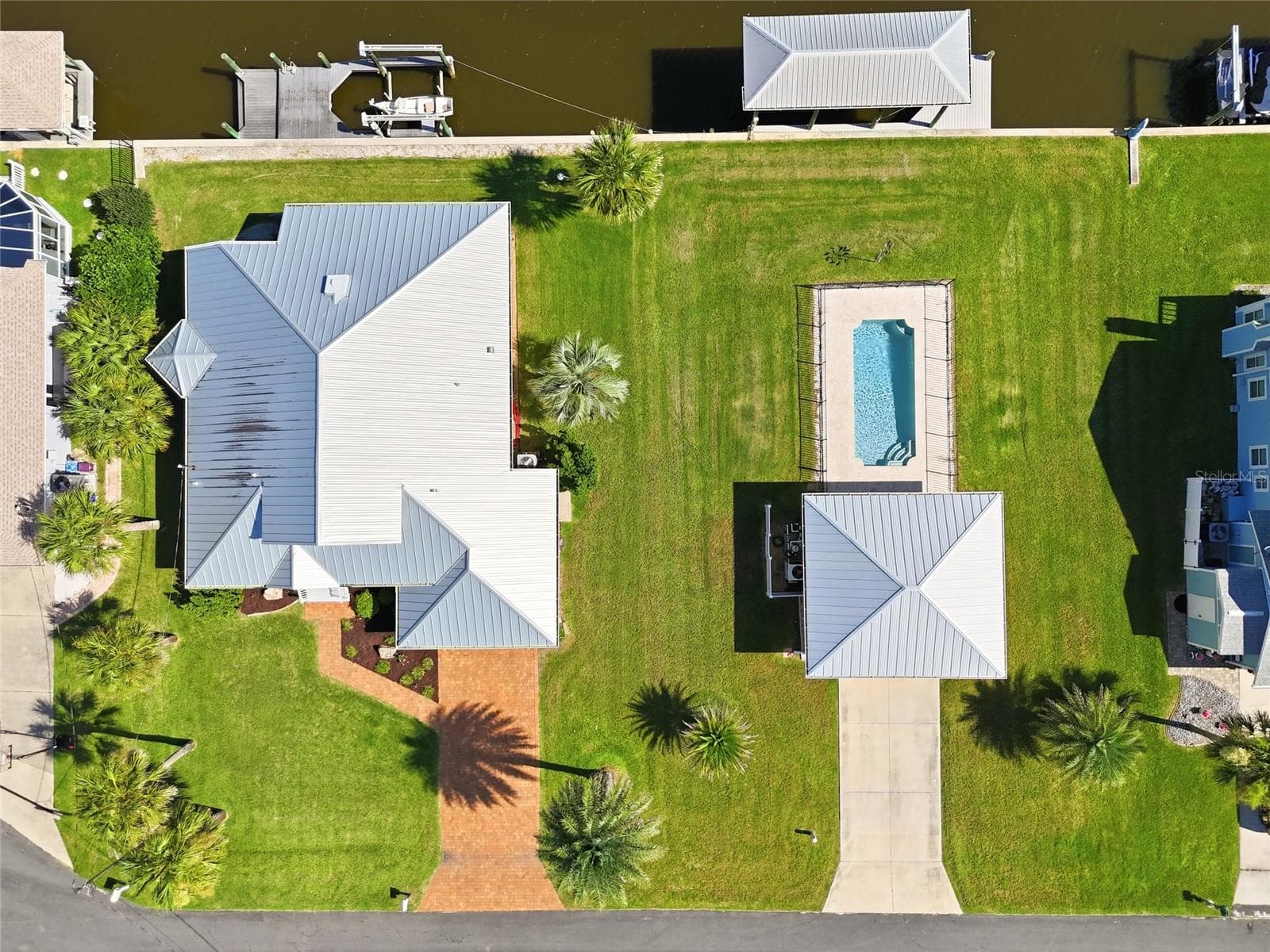 Aerial view (overhead) — Straight-down aerial view of the property showing the standing-seam metal roofline, brick paver walkway, backyard pool, detached poolside structure, and private dock with covered boat lift. - 342 N 12TH ST, FLAGLER BEACH
