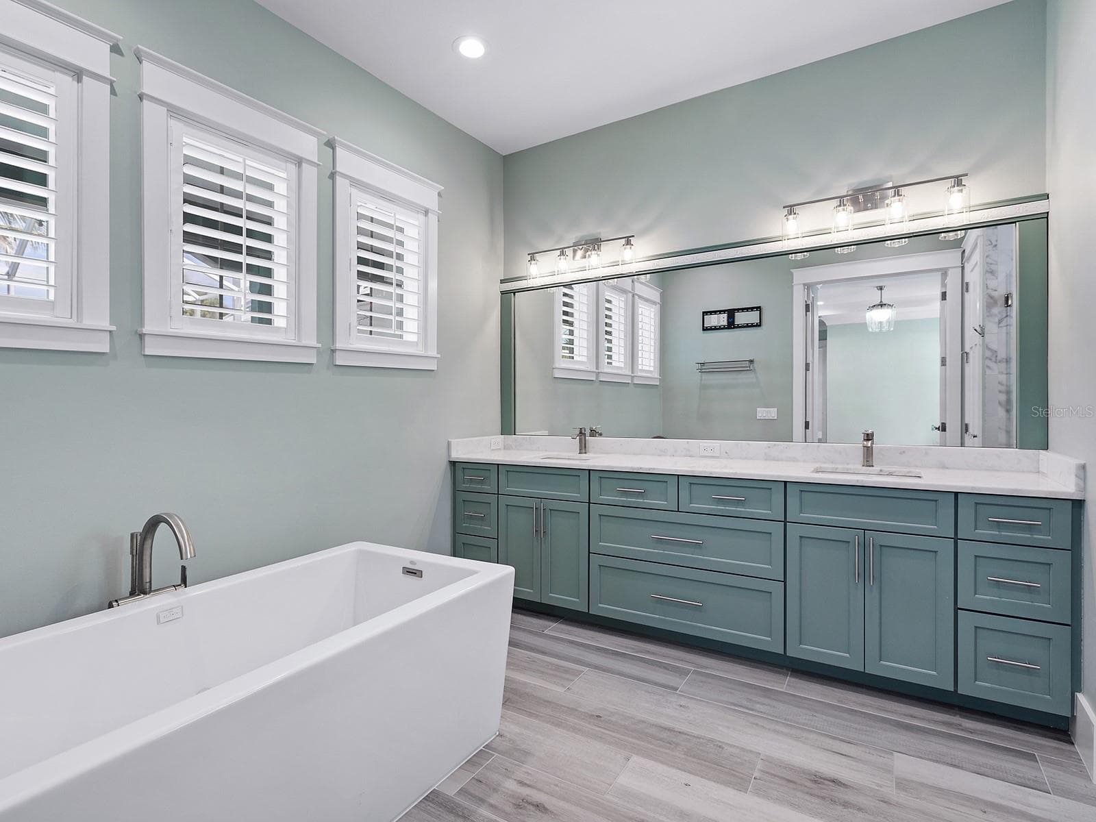 Main-level primary bath featuring a freestanding soaking tub, shaker vanity, and plantation shutters - 4024 11TH STREET CT W, PALMETTO