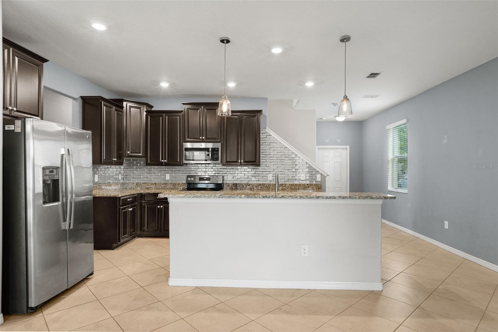 Kitchen — Spacious kitchen featuring granite countertops, stainless-steel appliances, dark cabinetry, breakfast bar seating, and pendant lighting. - 13728 REINDEER CIR, HUDSON