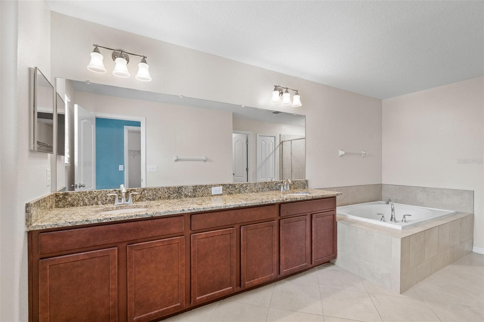Primary Bathroom – Spacious primary bathroom featuring a long dual-sink granite vanity, large mirror, tile flooring, and soaking tub. - 13728 REINDEER CIR, HUDSON